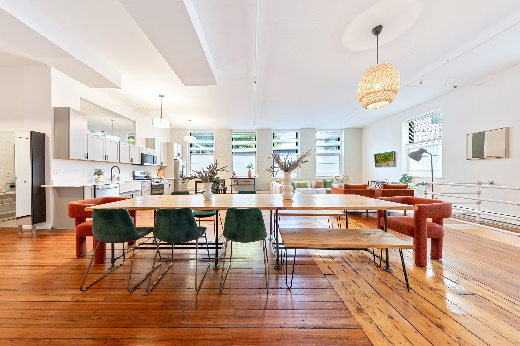 Open-plan loft dining area with a long wooden table, colorful chairs, and white kitchen cabinetry.