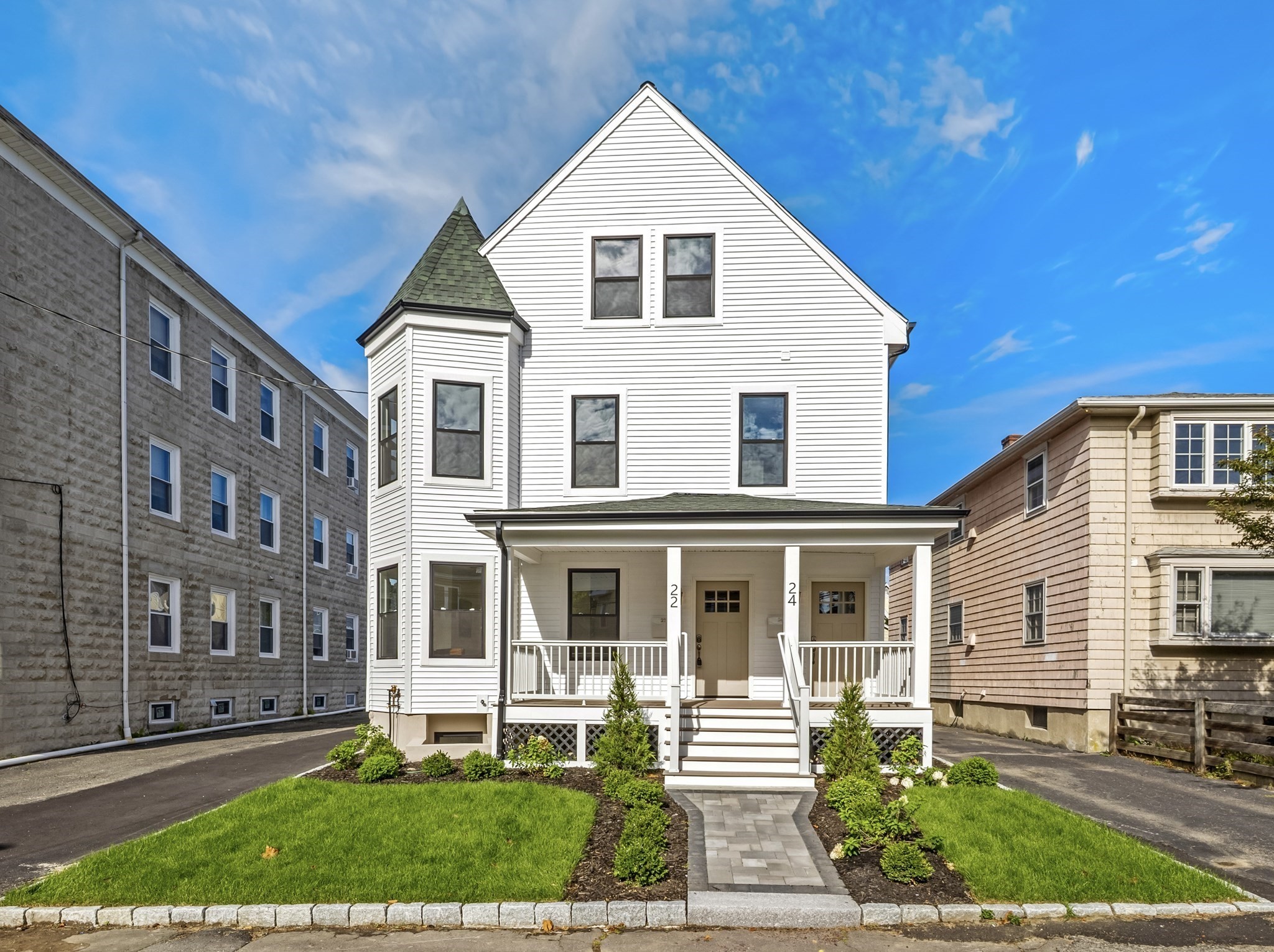 White two-entry home with a covered porch, turret, and landscaped front lawn.