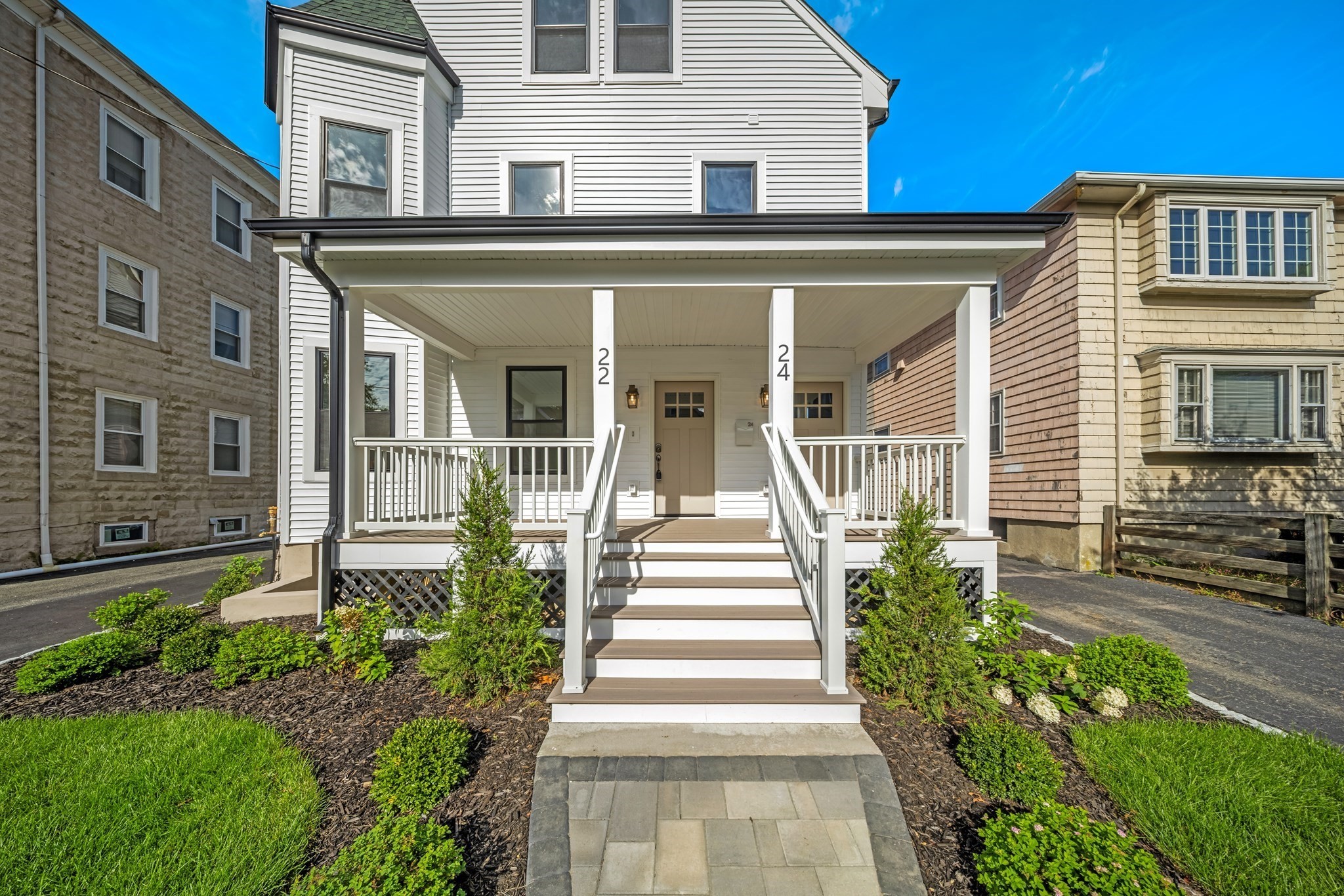 White two-story home with a covered porch, paired entrances, central steps, and landscaped shrubs.
