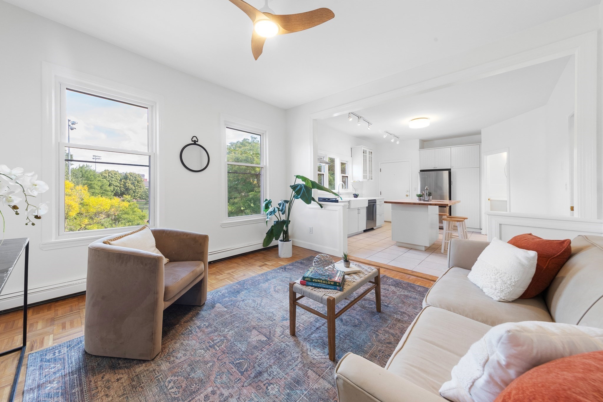 Living room opening into a bright white kitchen, with large windows and parquet flooring.