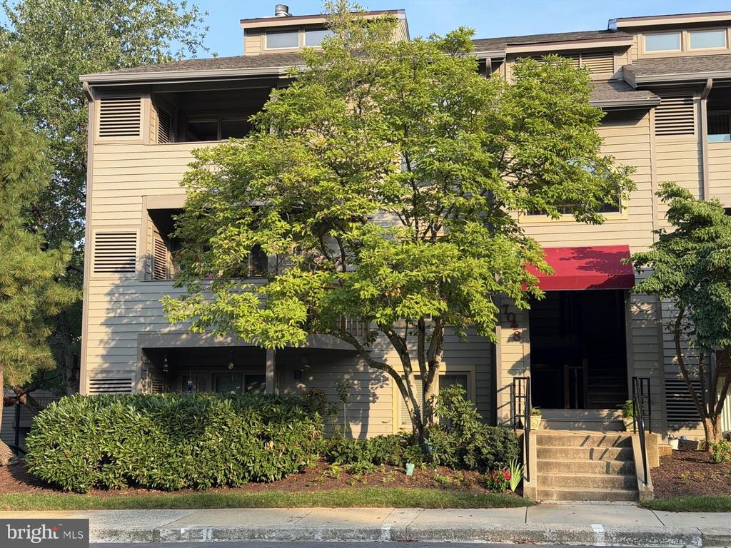 Tan residential building with a red entrance awning, front steps, and mature landscaping.