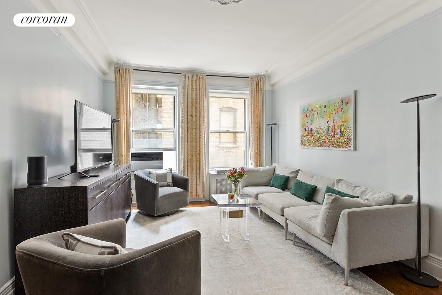 Furnished living room with a light sectional, tall curtained windows, and colorful wall art.