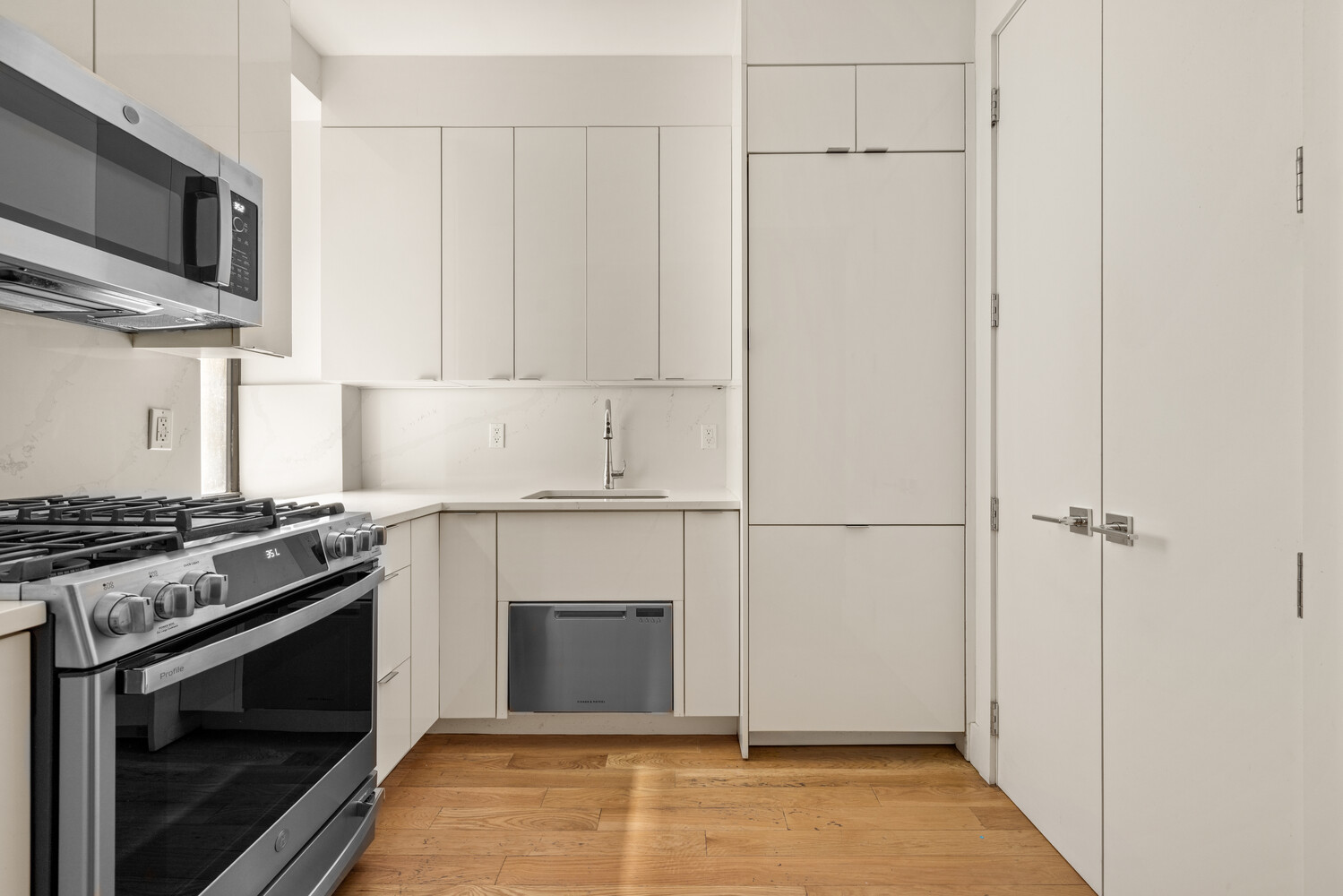 Modern kitchen with white cabinets, stainless steel appliances, and warm wood floors.
