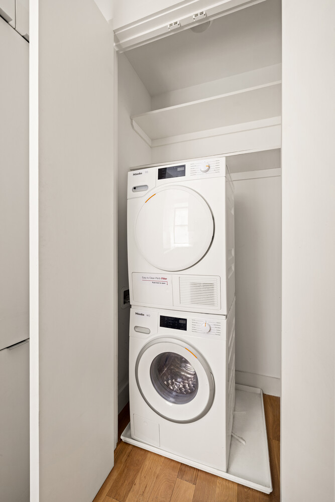Laundry closet with stacked white Miele washer and dryer beneath open shelves.