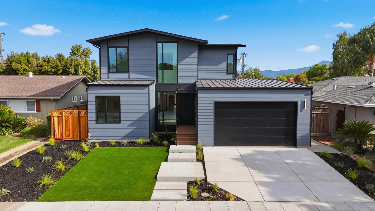 Modern gray two-story home with a black garage door, landscaped lawn, and mountain views.