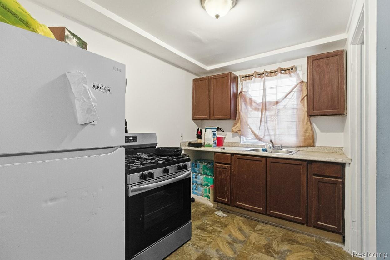 Kitchen with dark wood cabinets, a white refrigerator, gas range, and sink beneath a curtained window.