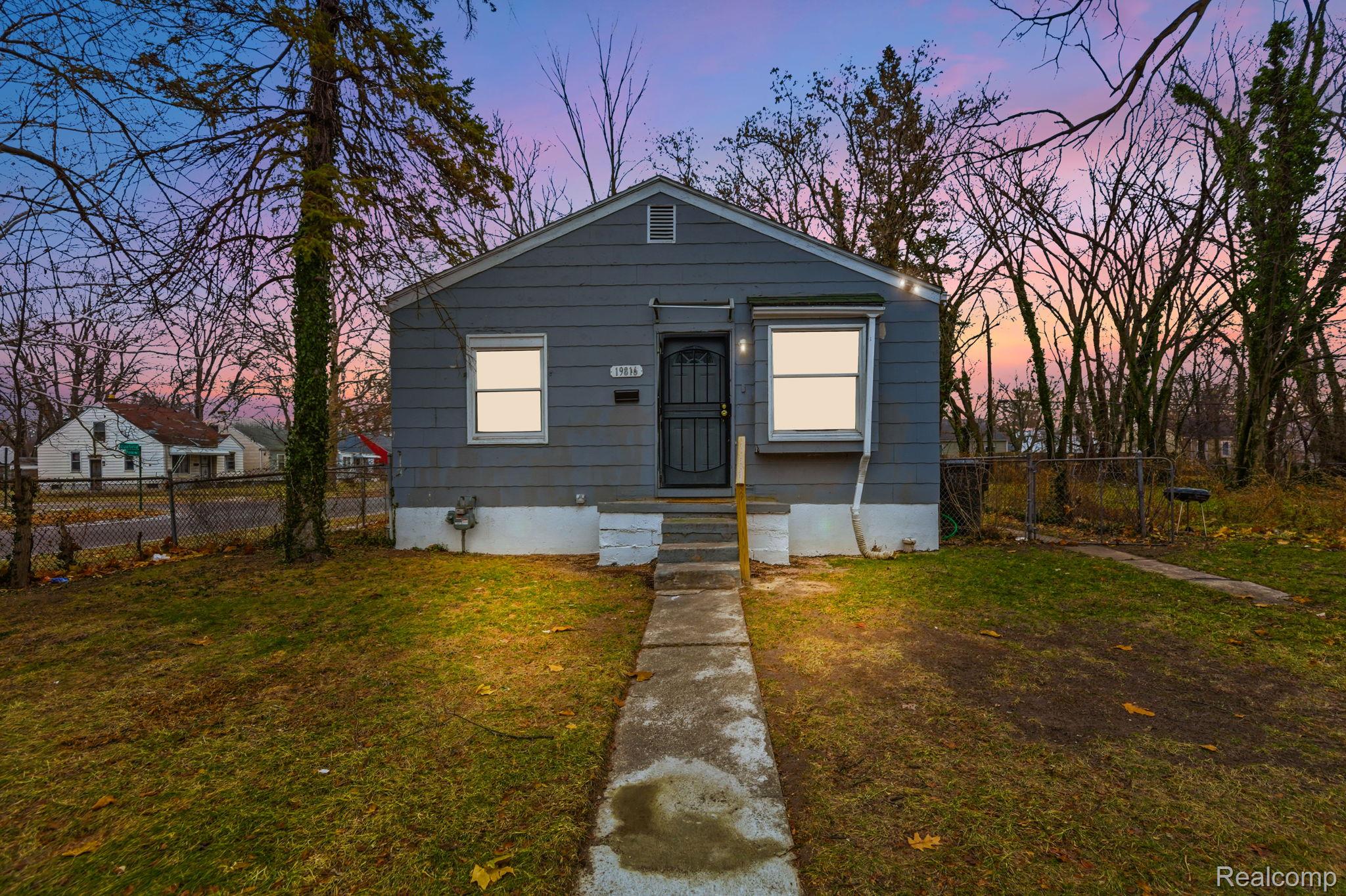 Small gray single-story house with front steps and a fenced yard at dusk.