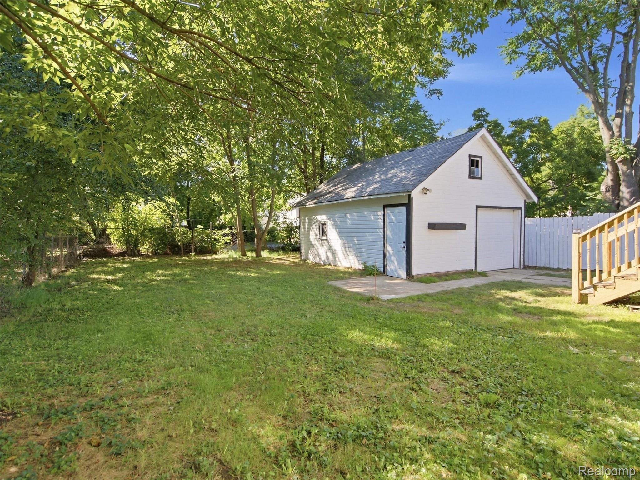Detached white garage in a tree-shaded backyard with a grassy lawn and white fence.