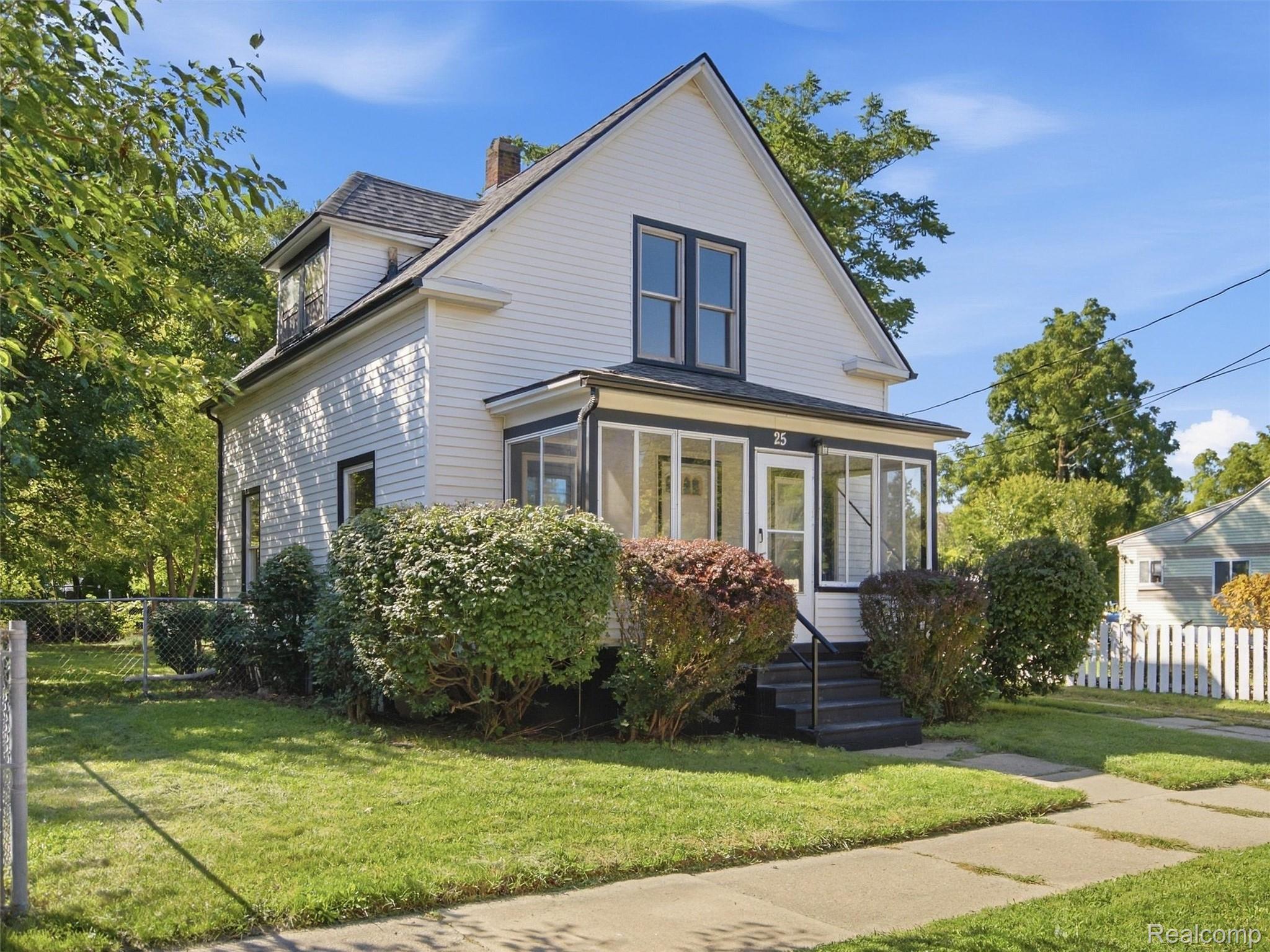 White two-story home with a steep gabled roof, enclosed porch, and landscaped front yard.