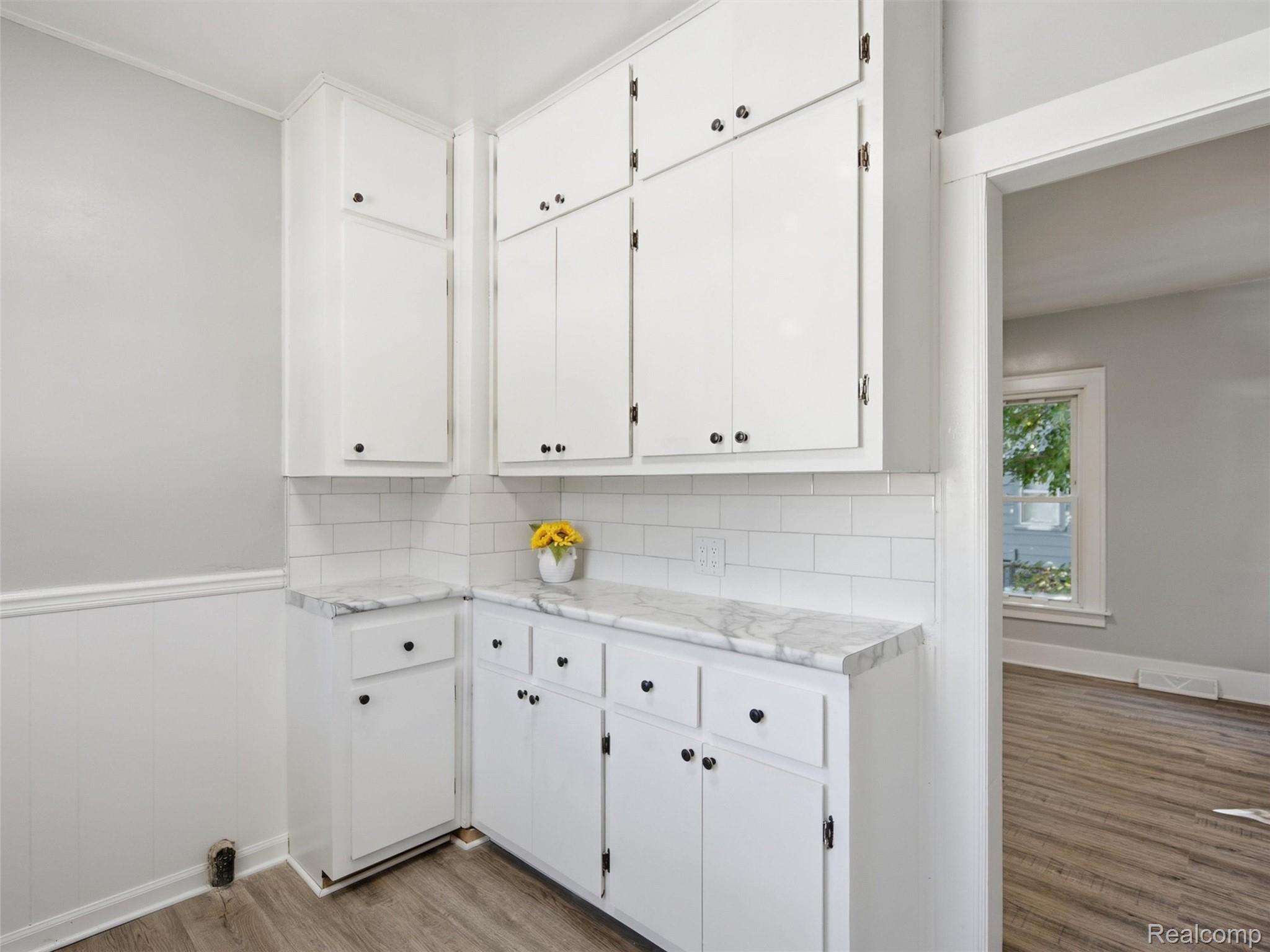Kitchen with white cabinets, marble-look counters, subway tile backsplash, and wood-look flooring.
