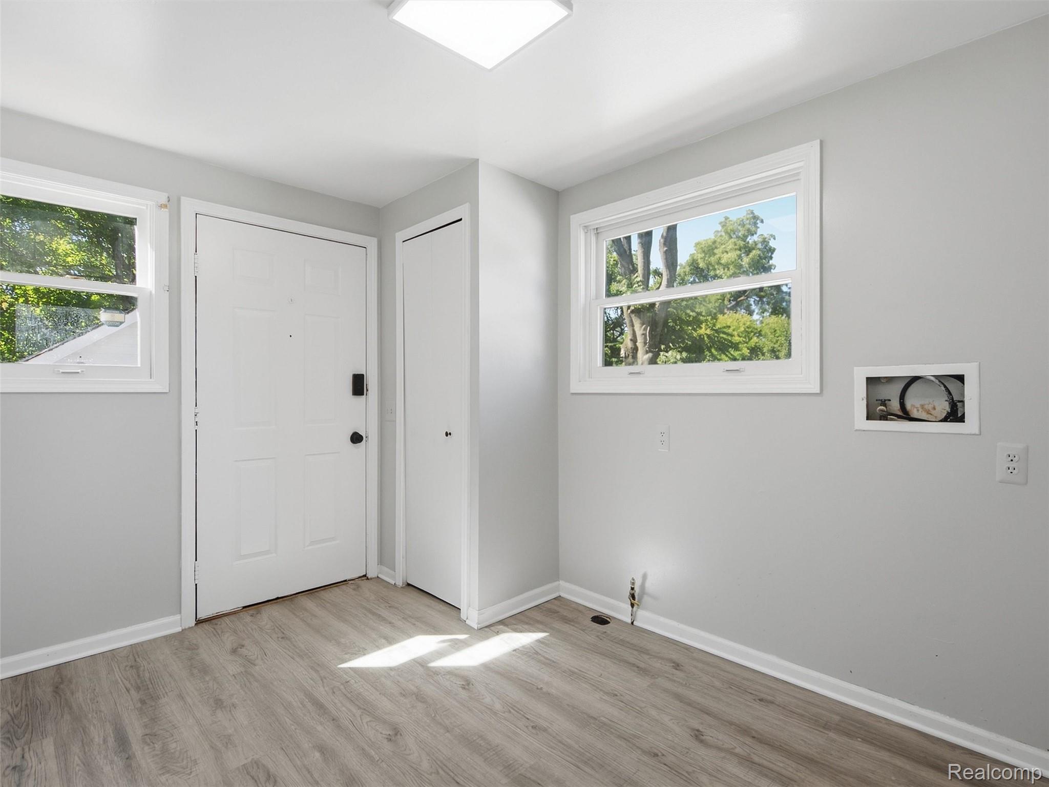 Vacant entry with a white front door, closet, two windows, and light wood-look flooring.