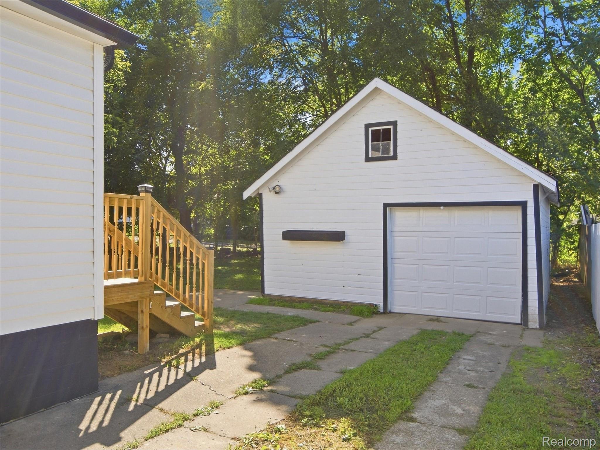 White detached garage beside a white-sided house, with wooden steps and a concrete driveway.