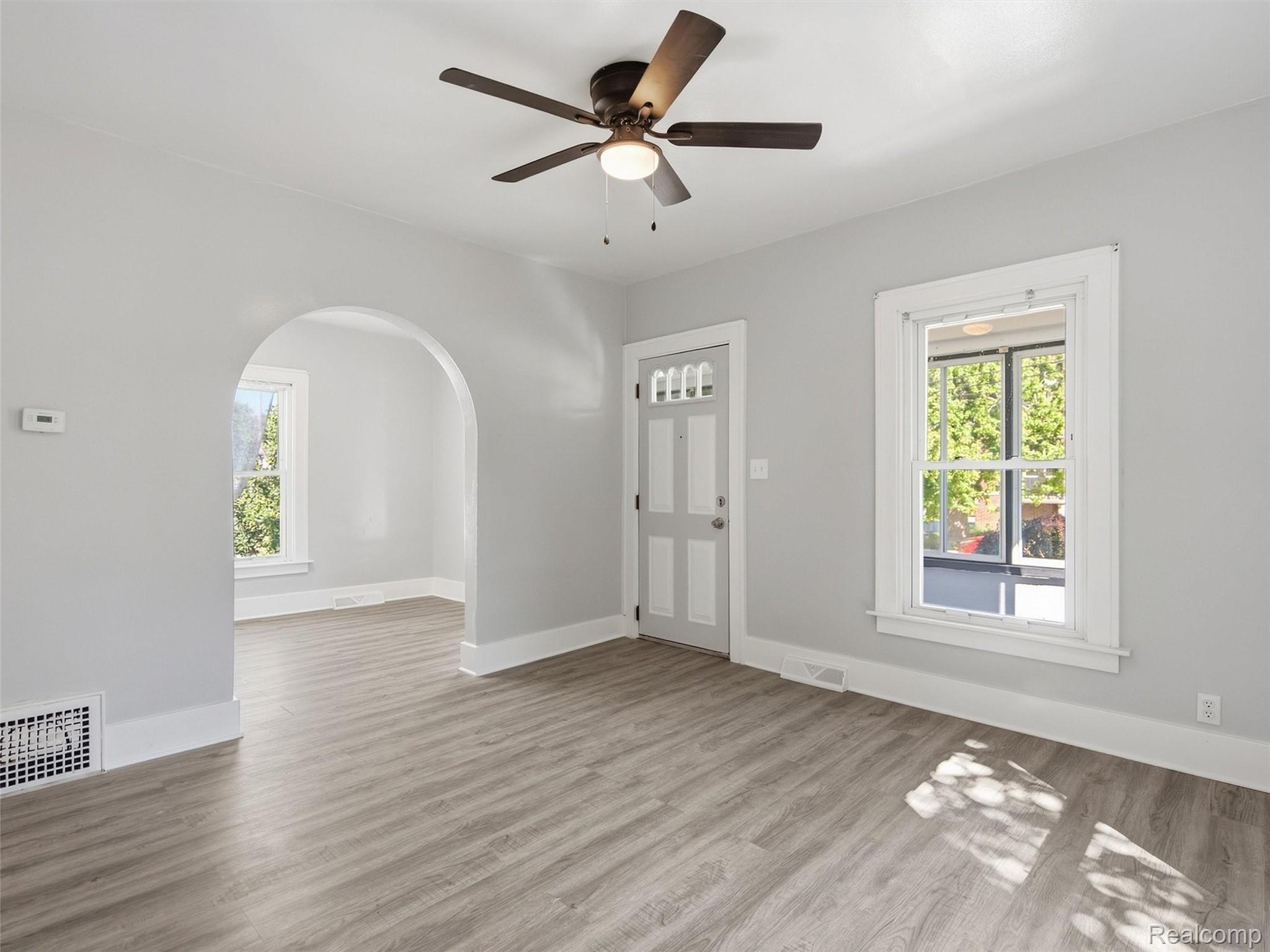 Empty room with gray wood-look flooring, a ceiling fan, and an arched opening.