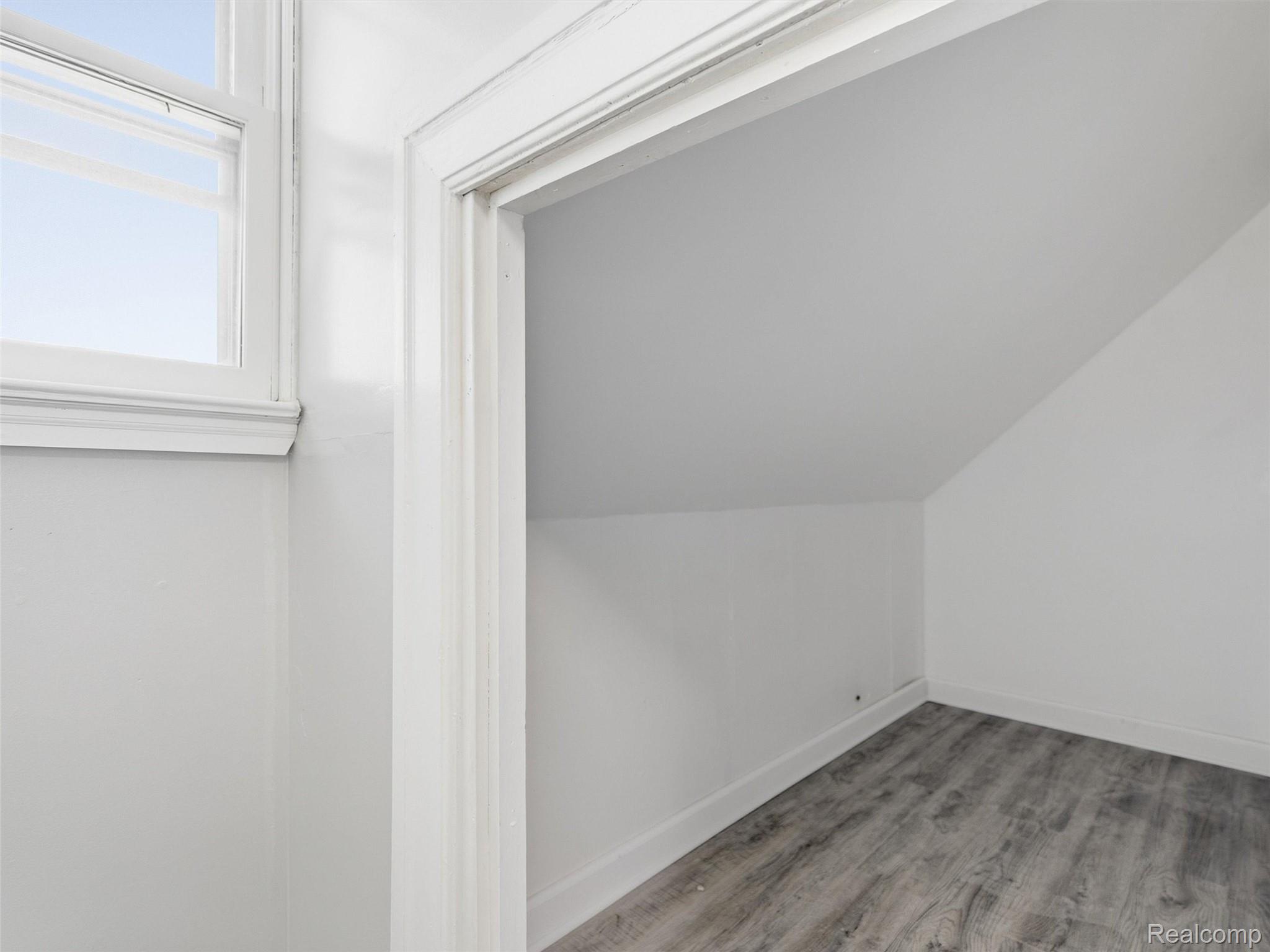 Empty room with a sloped ceiling, gray wood-look flooring, and a high window.