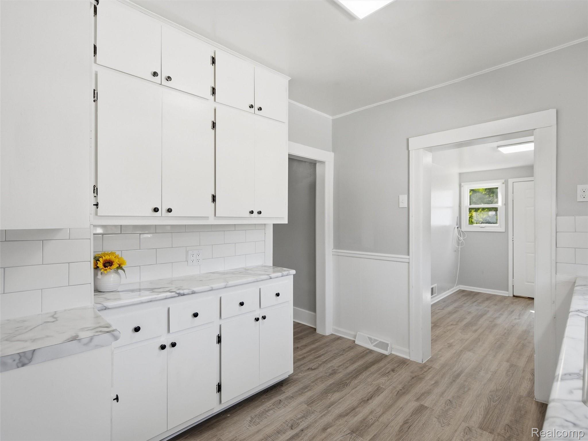 Vacant kitchen with white cabinetry, marble-look counters, subway tile backsplash, and a doorway to an adjoining room.