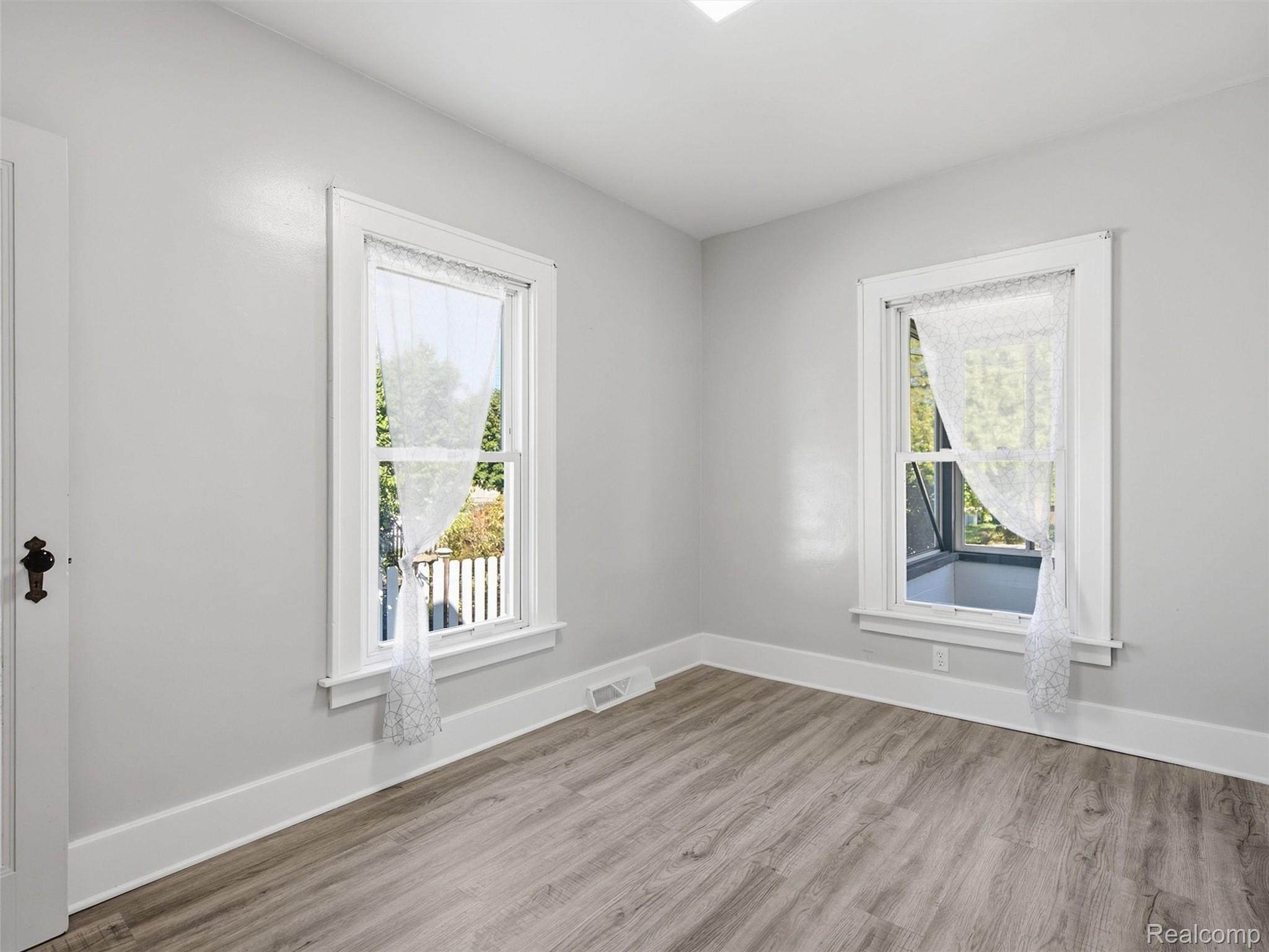 Empty room with wood-look flooring, gray walls, and two curtained windows.