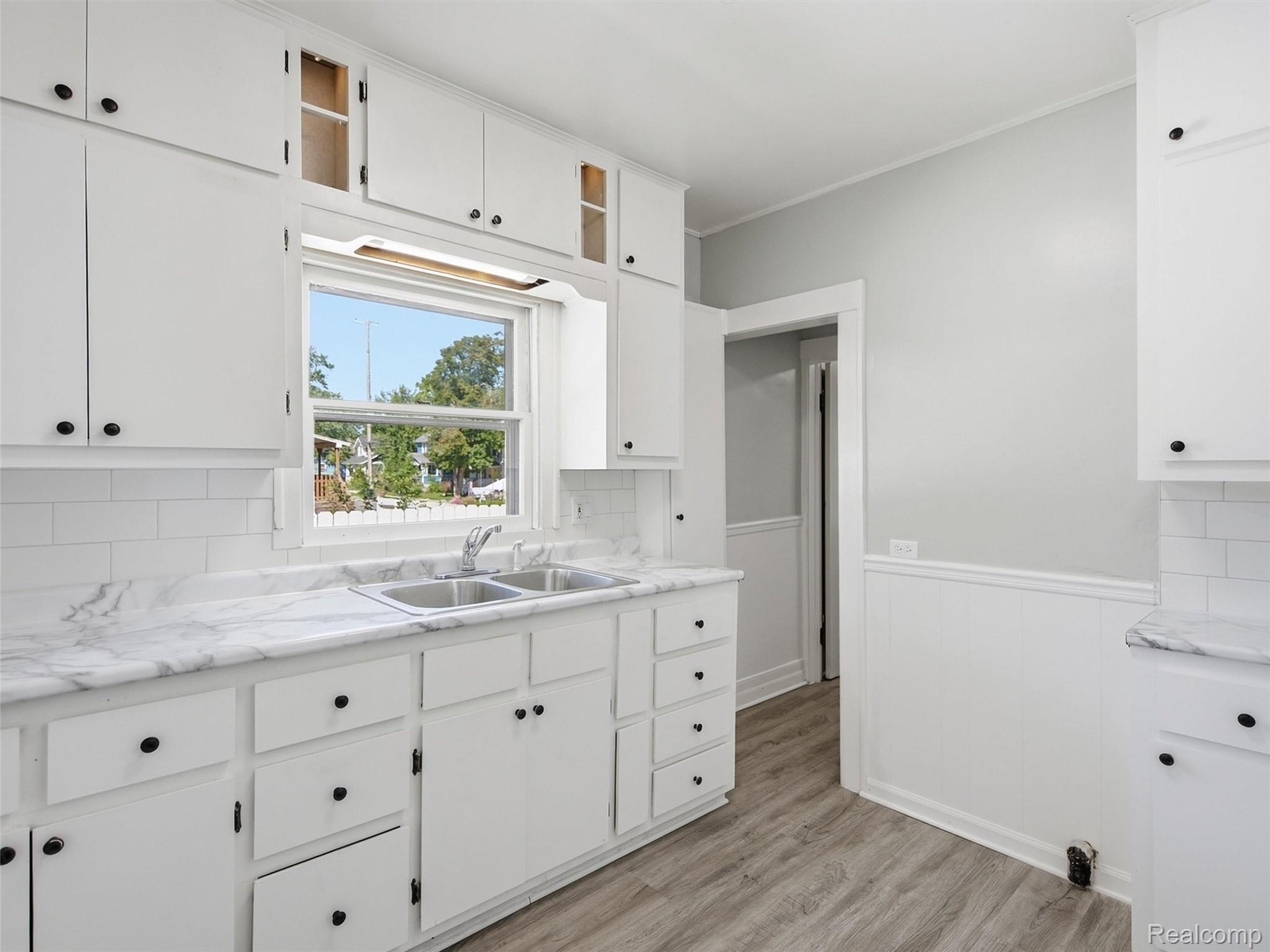 Kitchen with white cabinets, marble-look counters, and a double sink beneath a window.