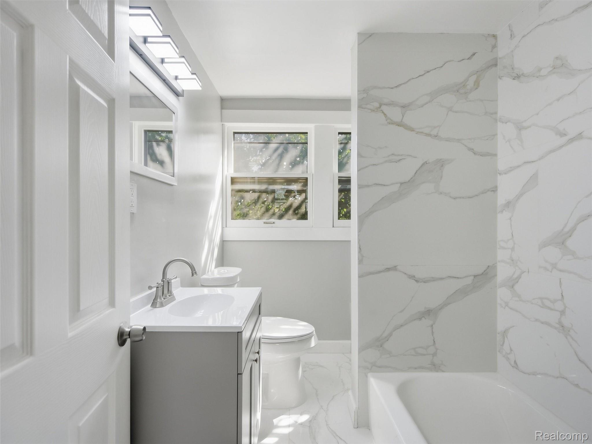 Bathroom with a gray vanity, white vessel sink, toilet, and marble-look tub surround.
