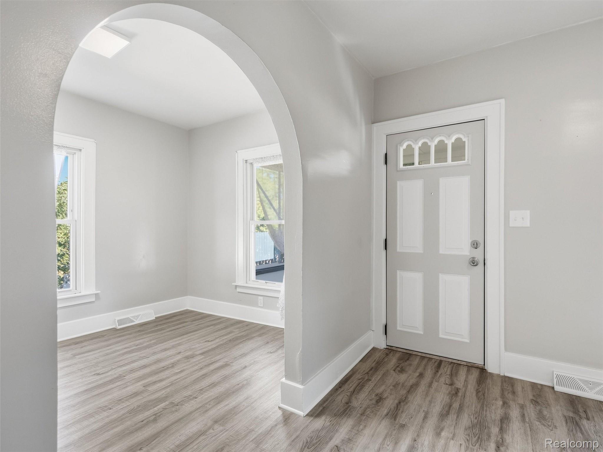 Vacant entryway with an arched opening, gray front door, and wood-look flooring.