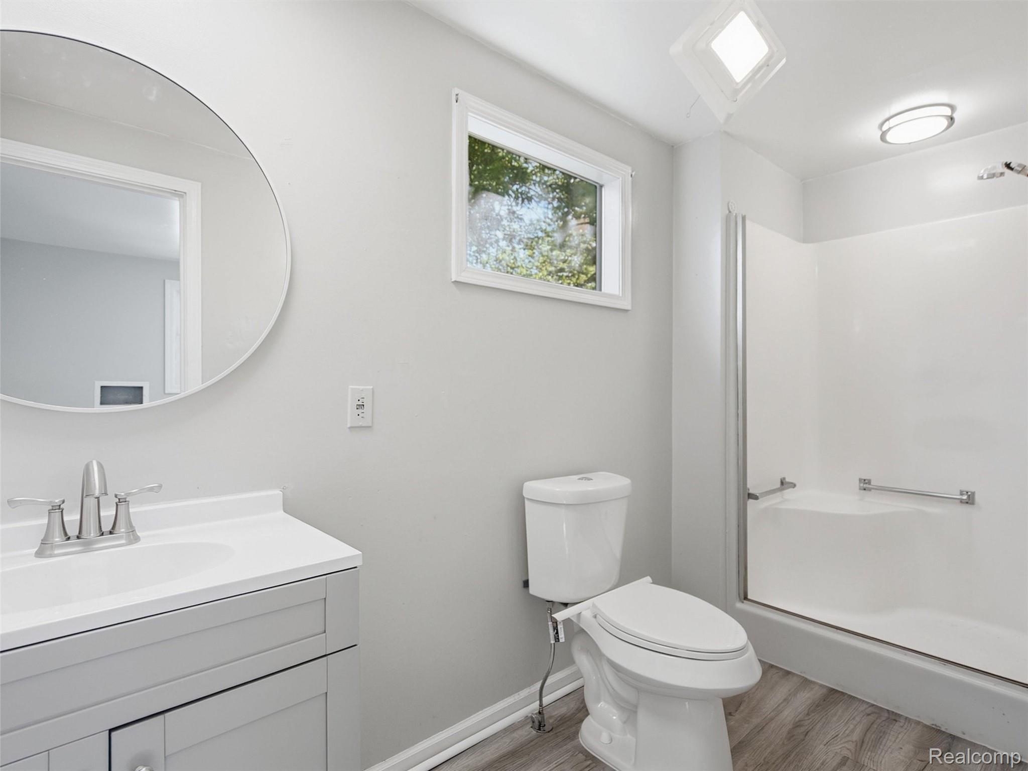 Bright bathroom with a white vanity, toilet, and tub behind a glass shower screen.
