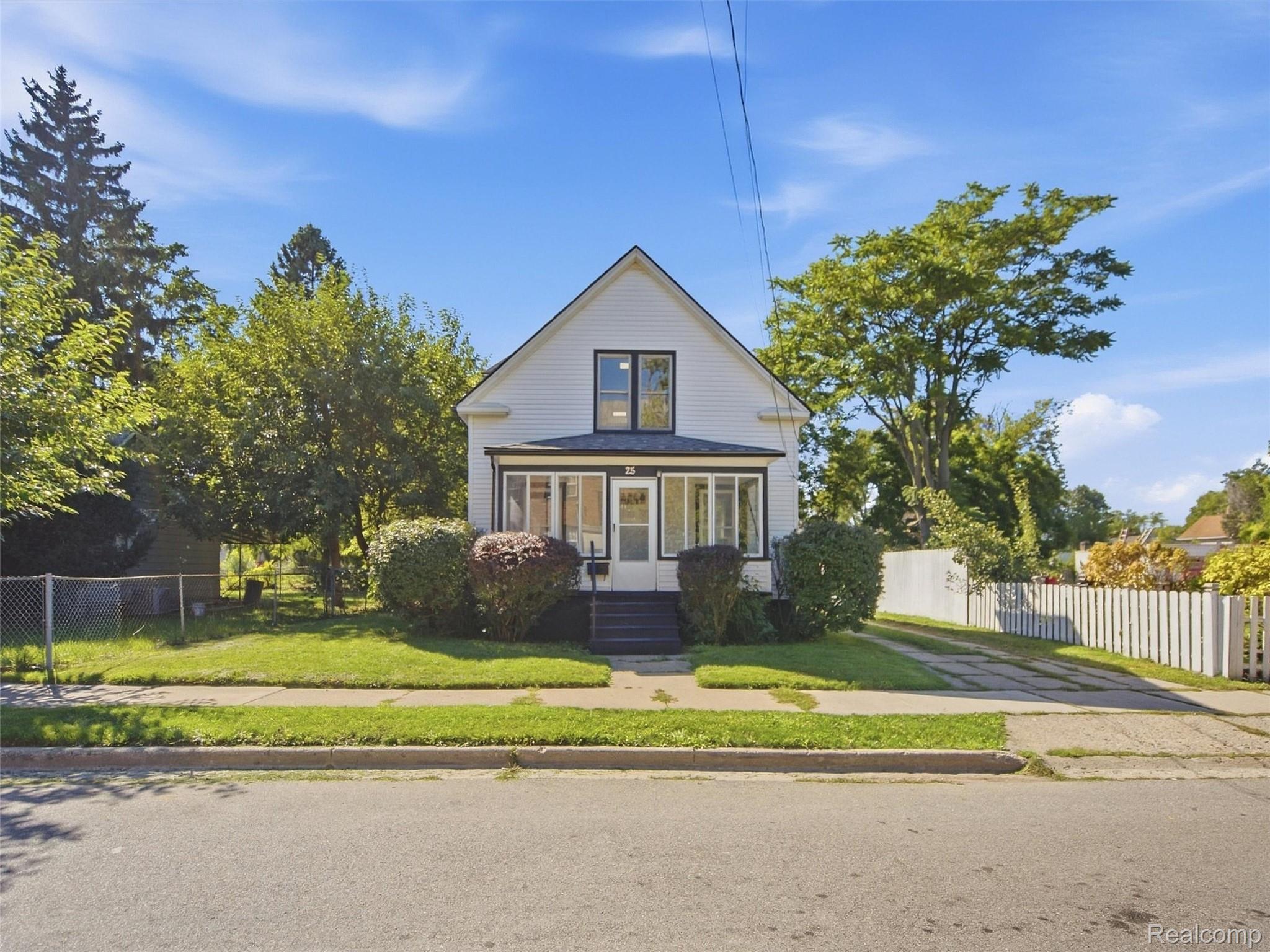 White gabled house with a glass-enclosed front porch, lawn, mature trees, and side driveway.