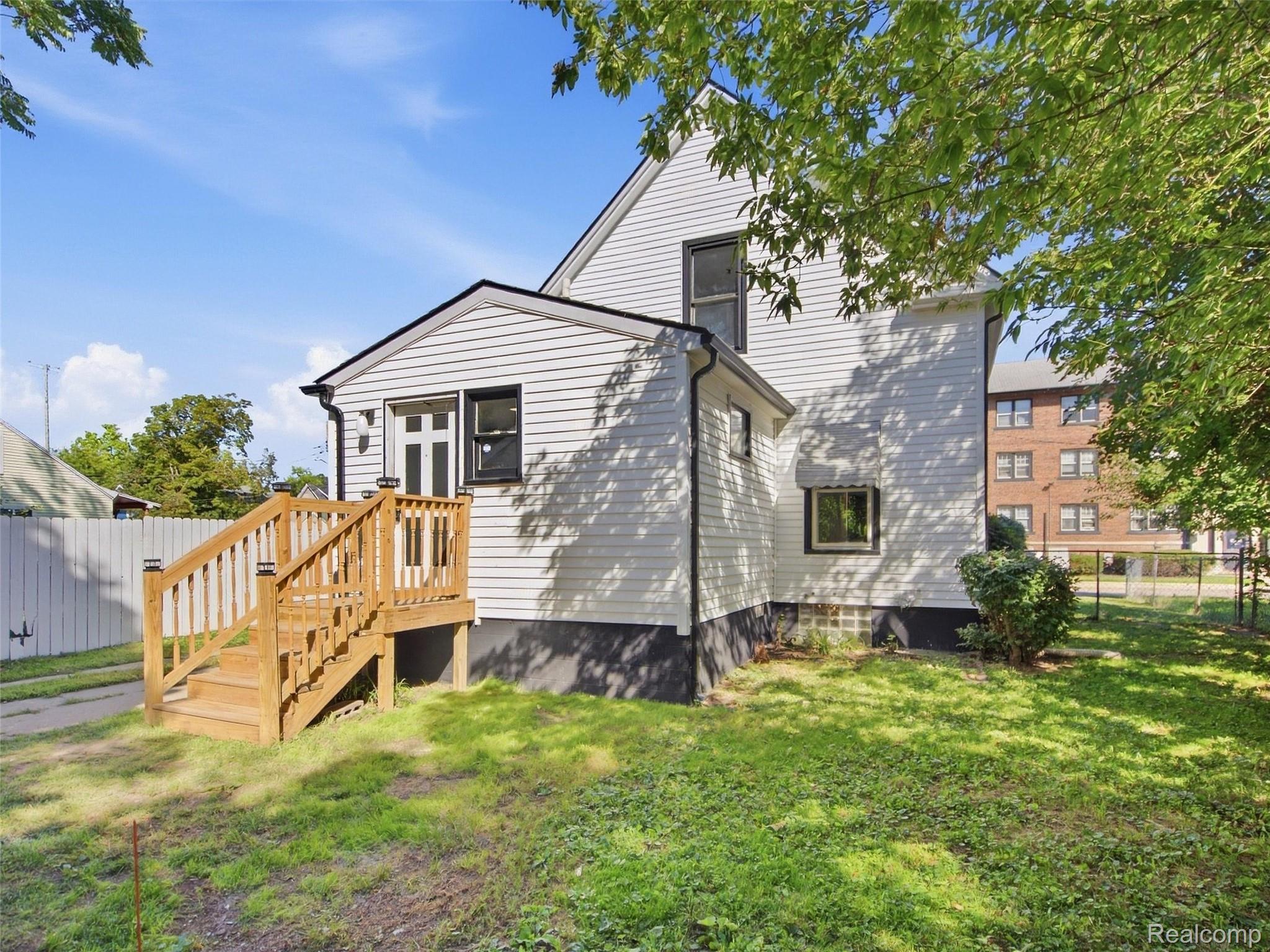 White two-story house with a raised wooden entry deck and stairs in a leafy yard.
