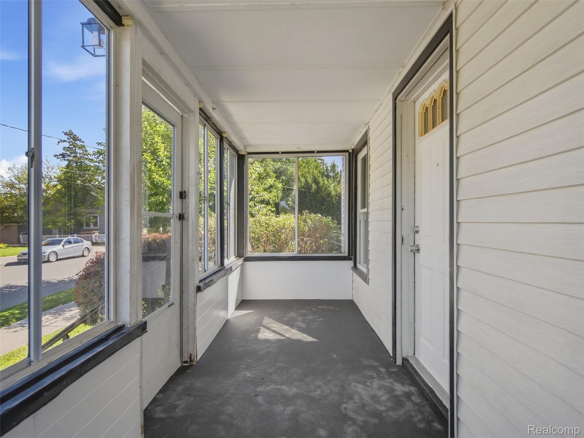 Enclosed front porch with large windows, white siding, and a front door.