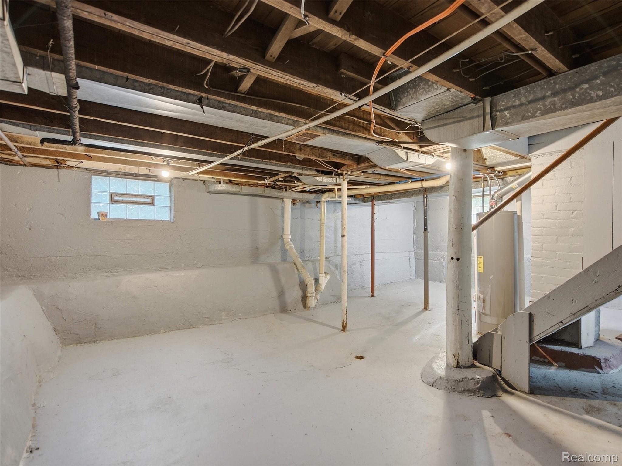 Unfinished basement with exposed joists and ductwork, utility pipes, and a small glass-block window.