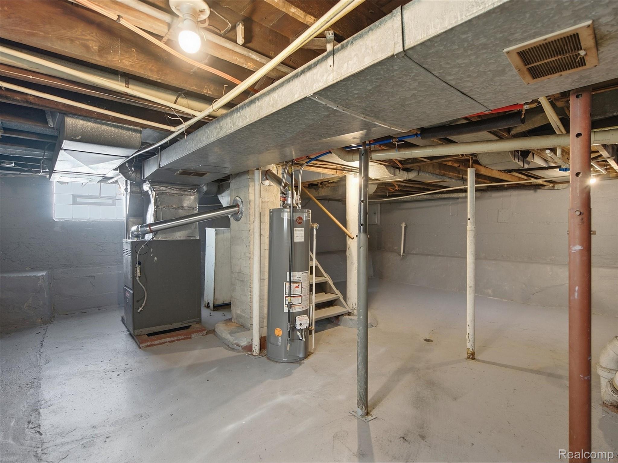 Unfinished basement with exposed ductwork, a furnace, water heater, and support posts.