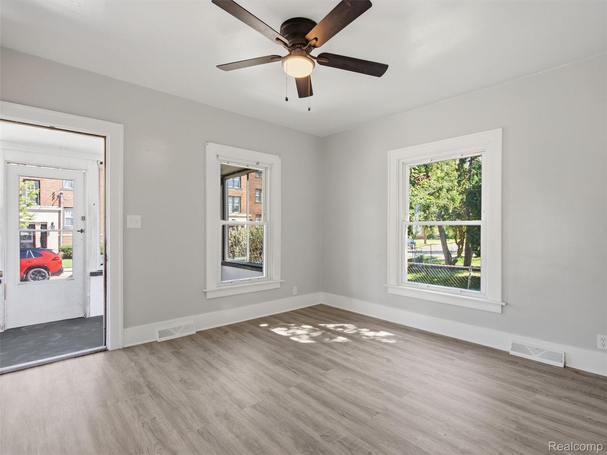 Empty room with light wood-look flooring, white-trimmed windows, and a ceiling fan.