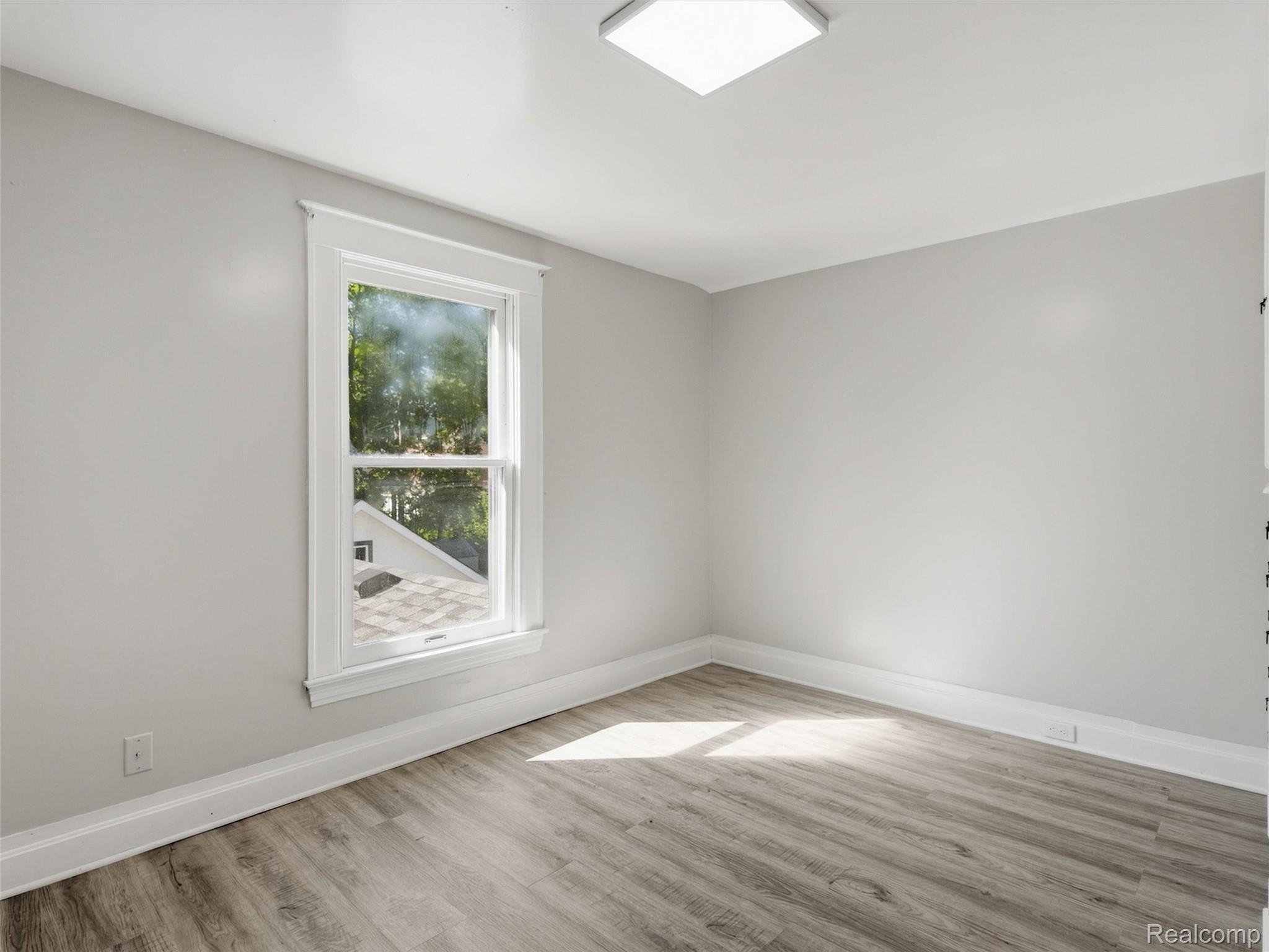 Empty room with gray wood-look flooring, white trim, and a large window overlooking trees.