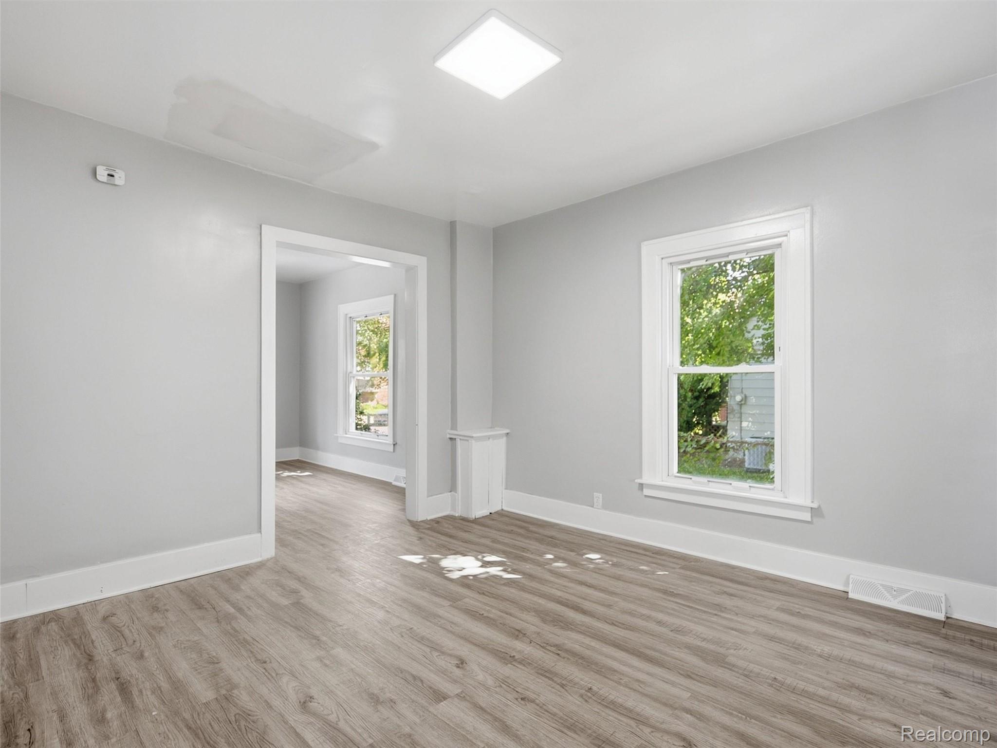 Empty gray room with wood-look flooring, a large window, and a wide doorway to another room.