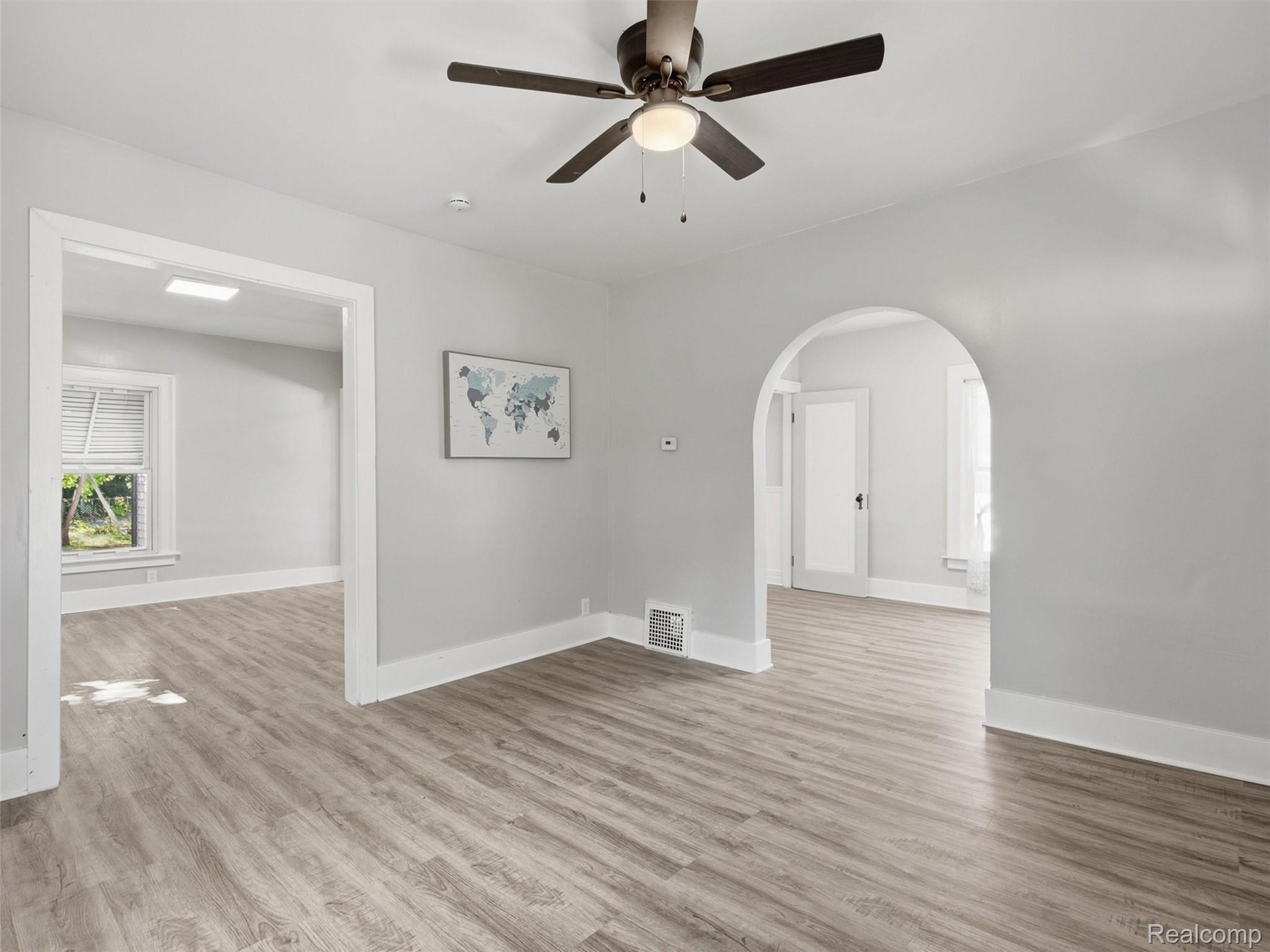 Empty living room with wood-look flooring, a ceiling fan, and an arched hallway opening.