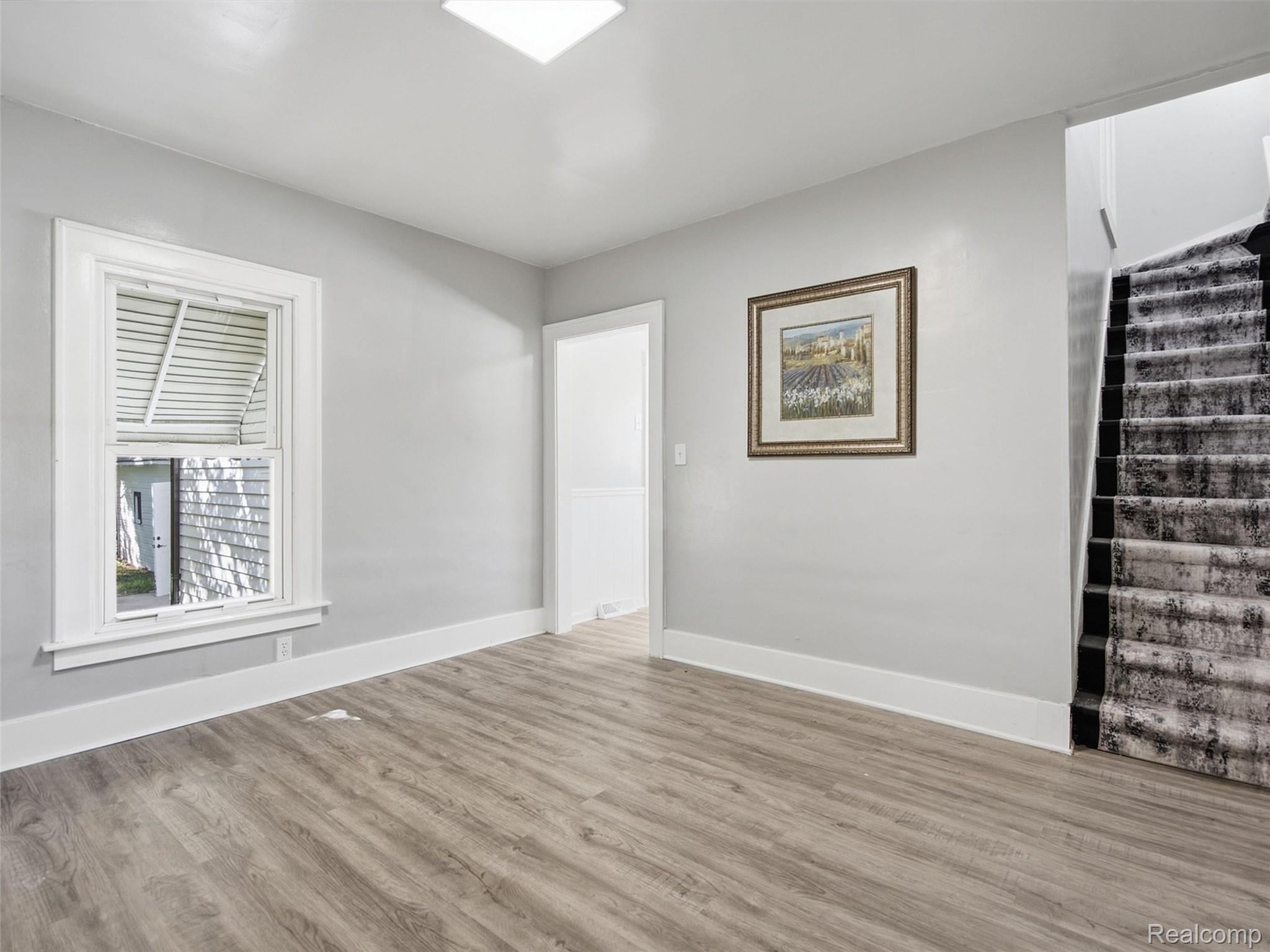 Empty room with wood-look flooring, a shuttered window, and carpeted staircase.
