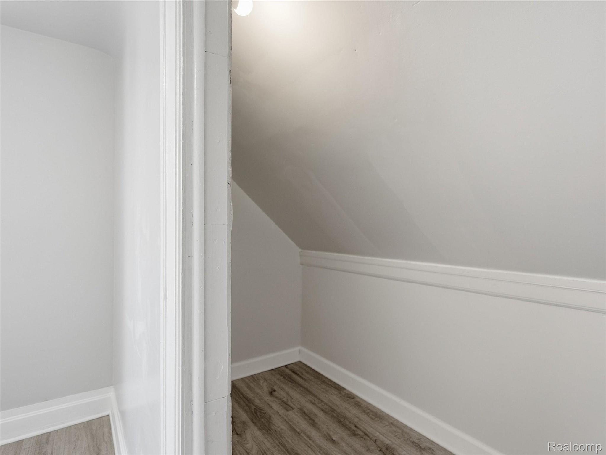 Small empty room with a sloped ceiling, white trim and wood-look flooring.