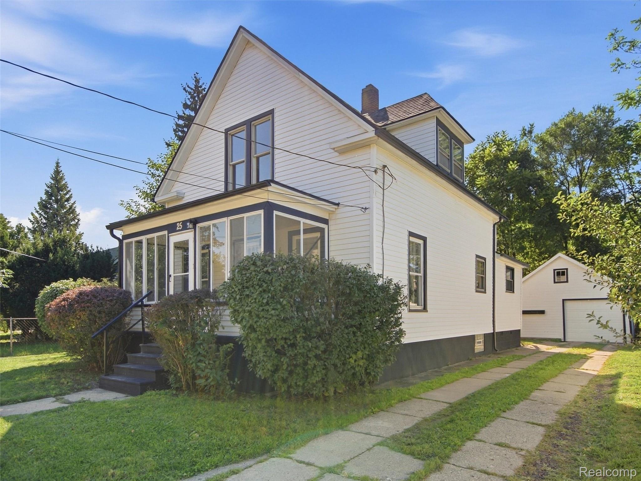 White two-story house with a glass-enclosed porch, mature shrubs, and detached garage.
