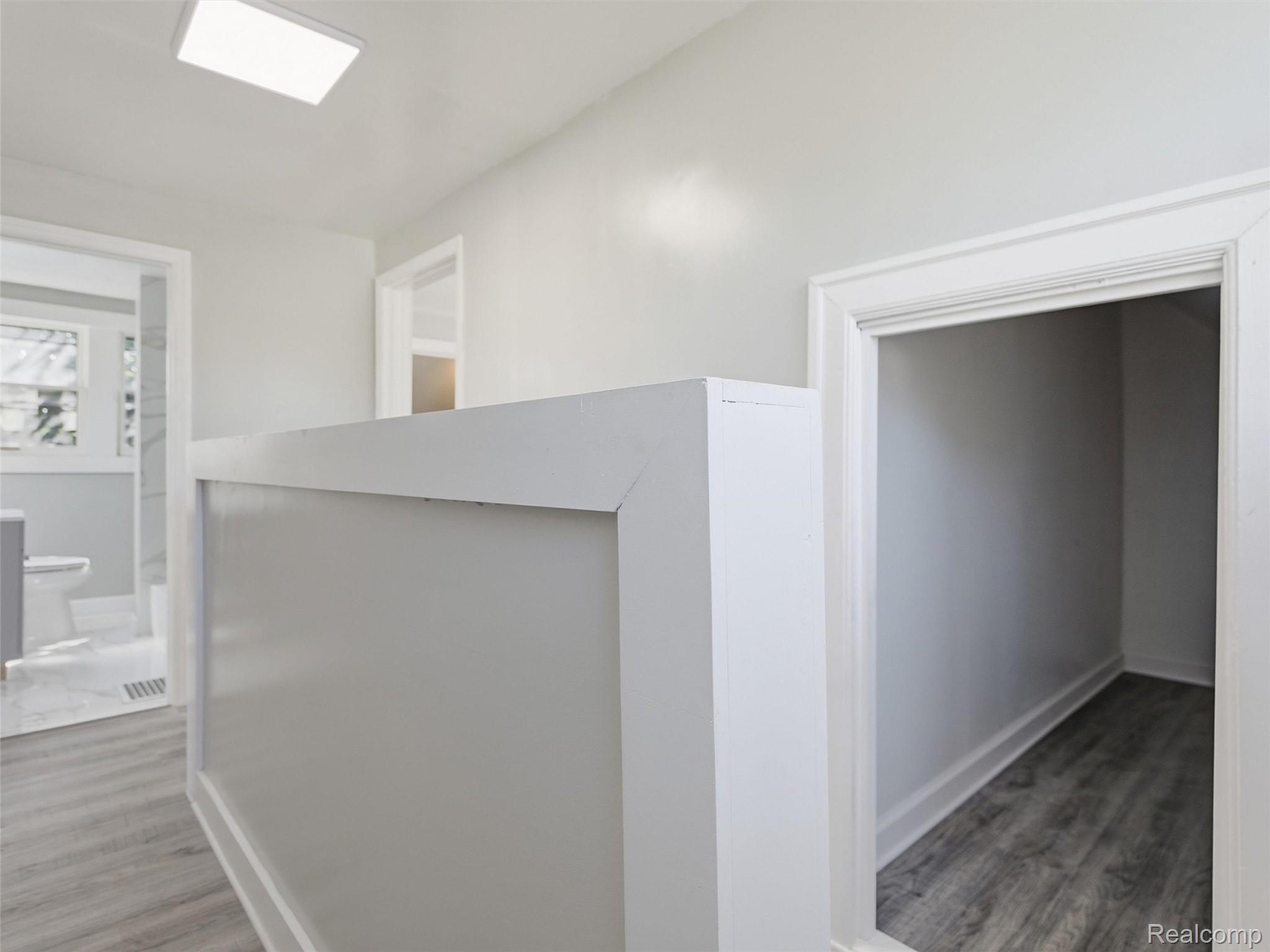 Interior landing with a white half wall, hallway opening, and bathroom doorway.