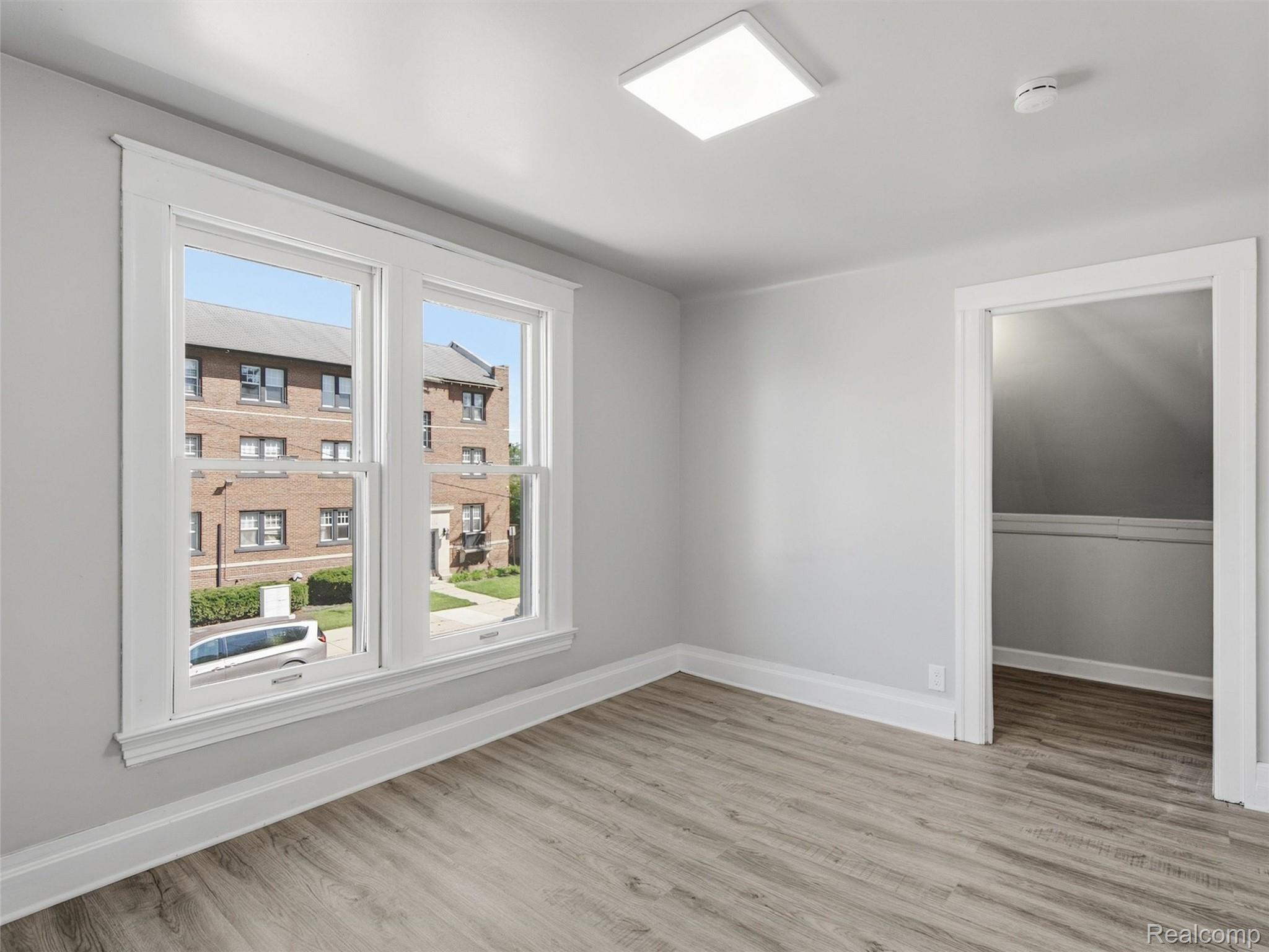 Empty room with two large windows, gray walls, and wood-look flooring.