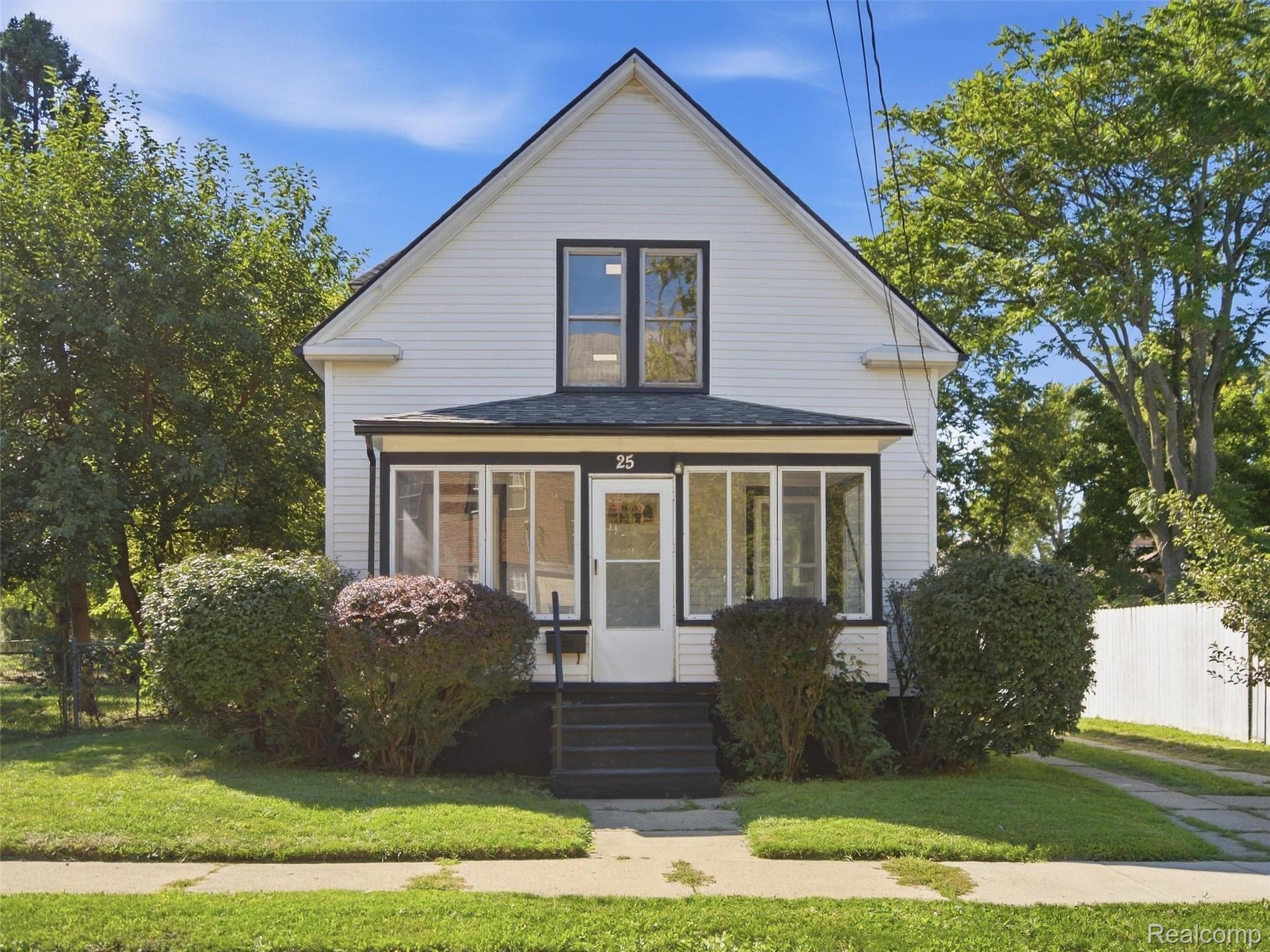 White two-story gabled house with a glass-enclosed front porch and mature landscaping.