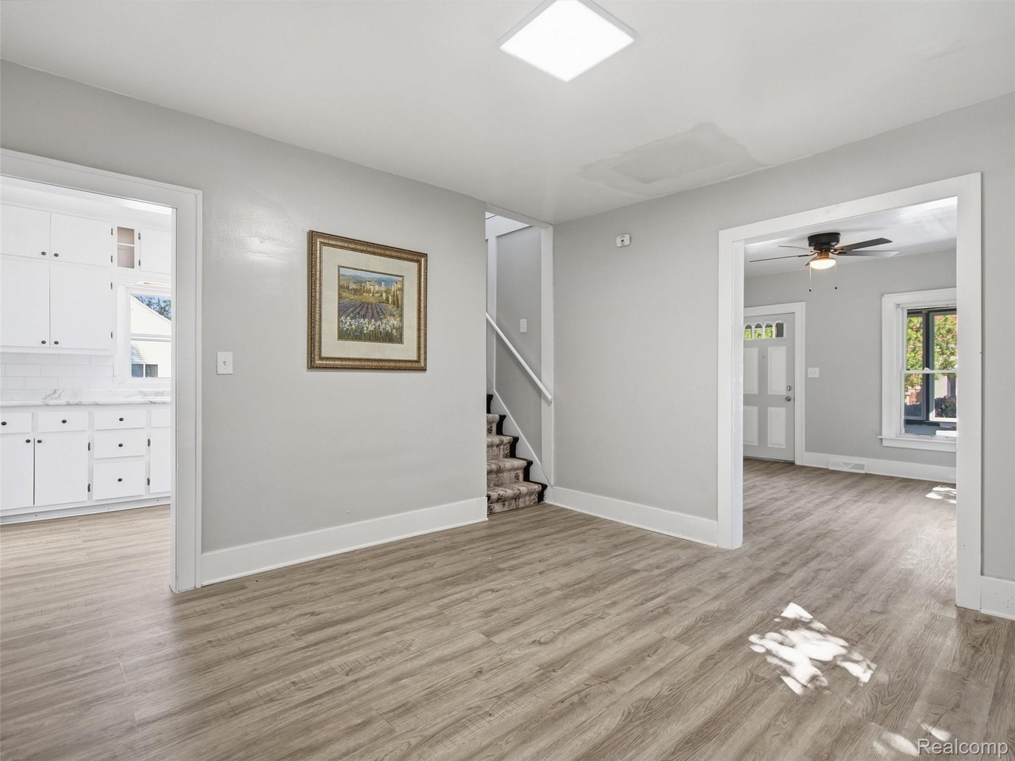 Open entry with wood-look flooring, carpeted stairs, and views into the kitchen and front room.