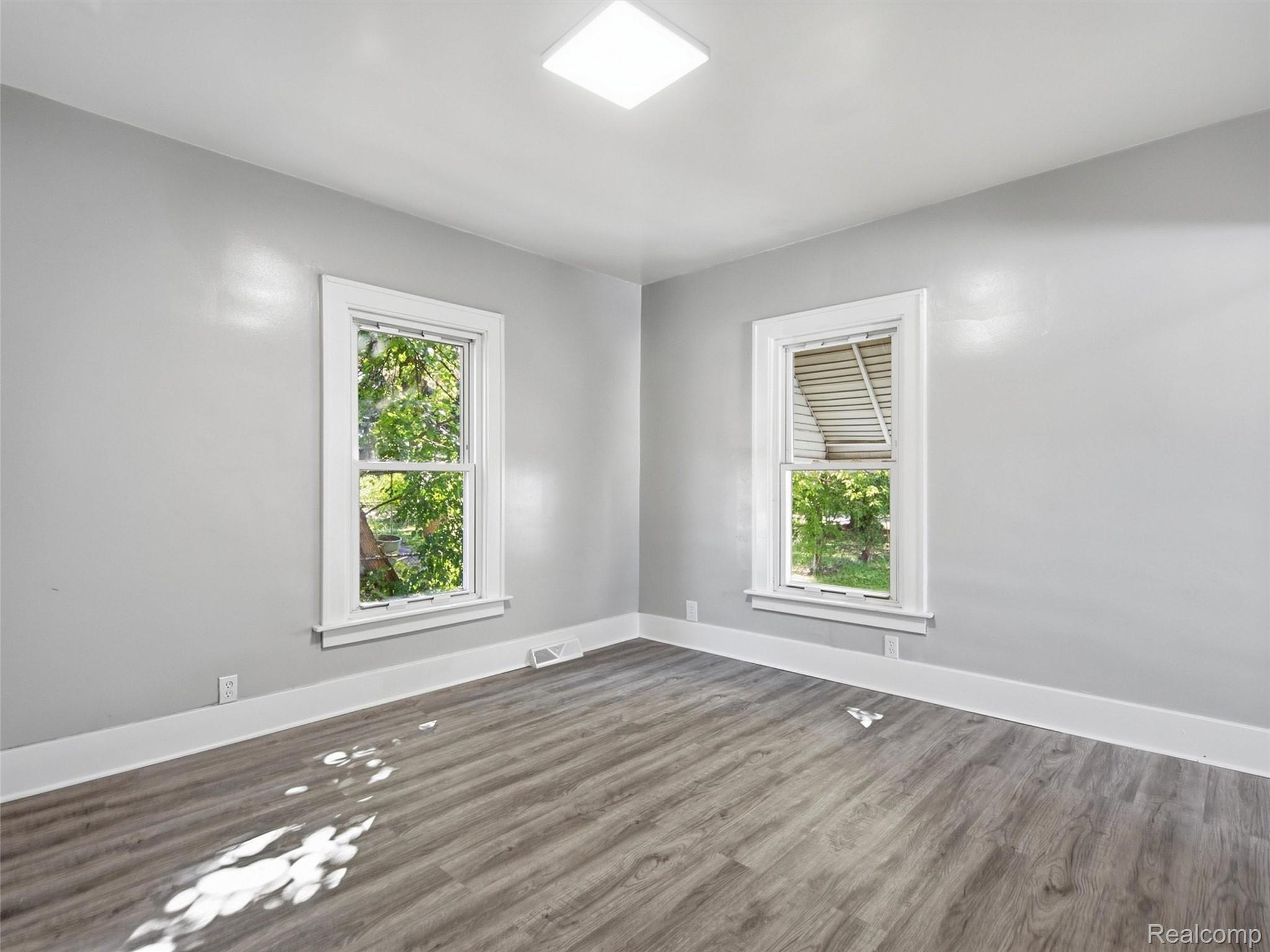 Empty room with gray wood-look flooring, two white-trimmed windows, and light gray walls.