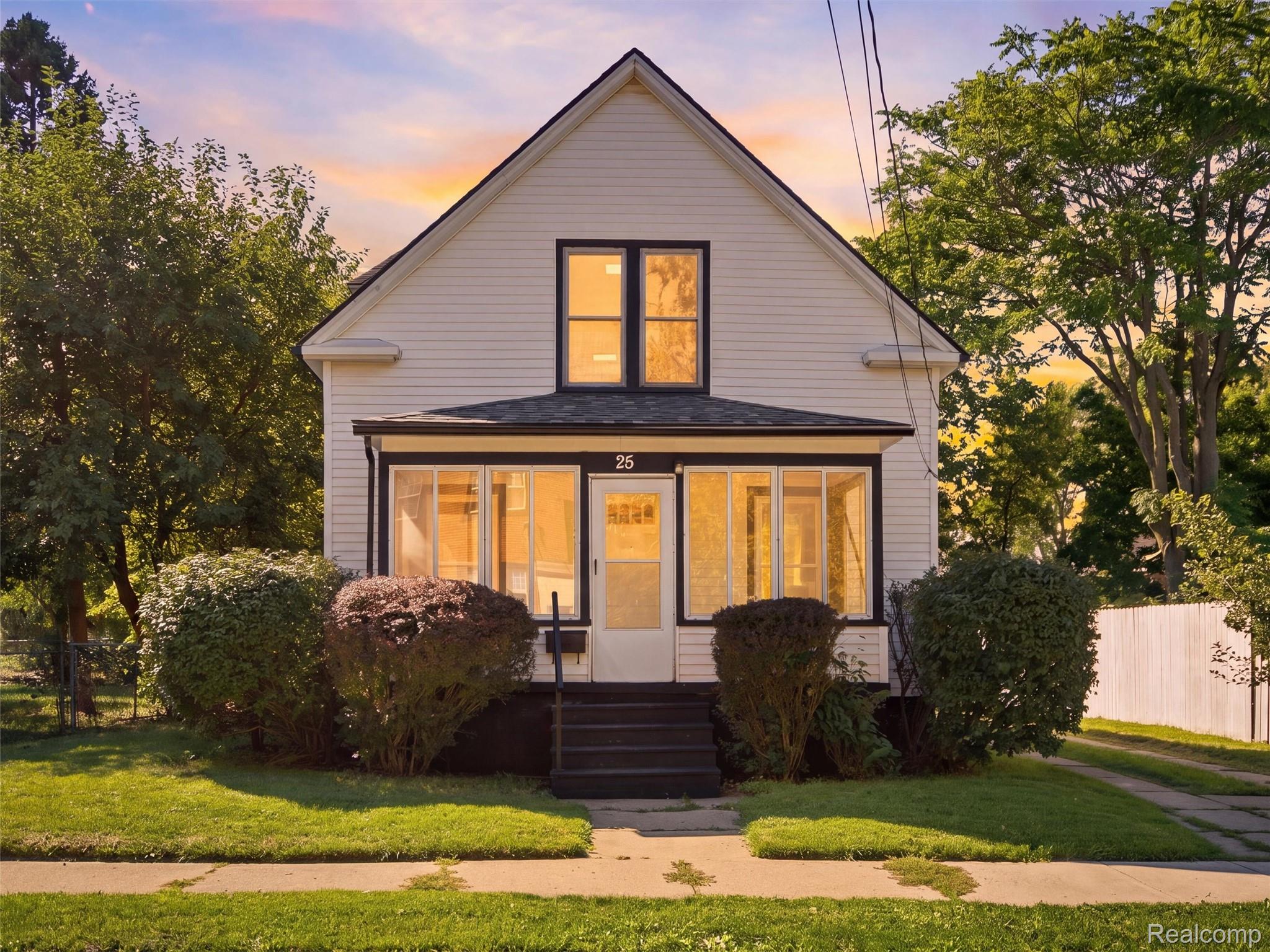 White two-story house with a glass-enclosed porch and front steps in warm evening light.