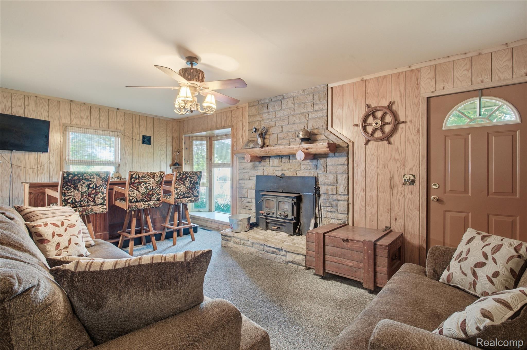 Living room with a stone fireplace and wood stove, wood-paneled walls, and brown sofas.