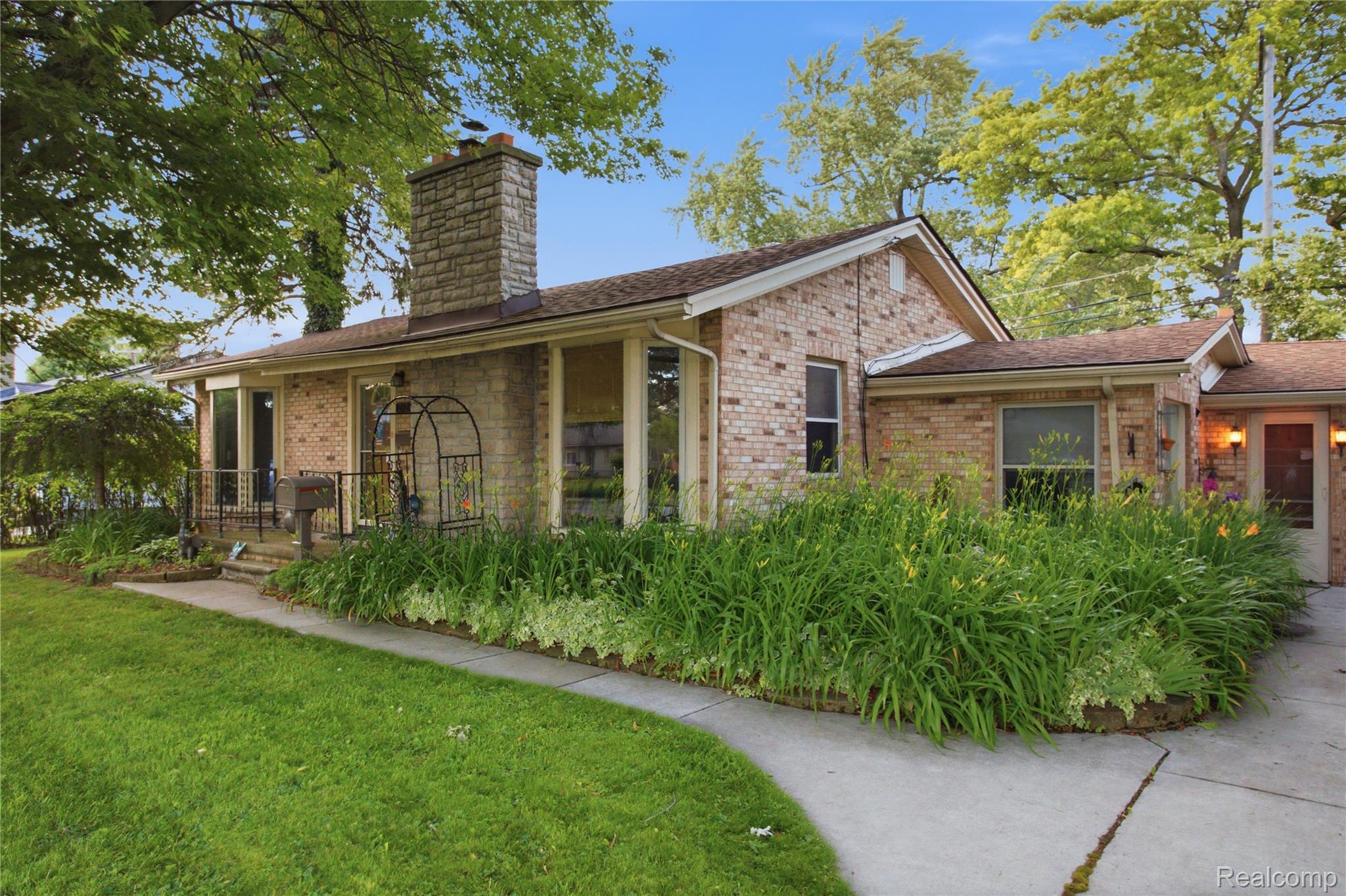 Brick home with a stone chimney, lush landscaping, and a curved walkway to the entrance.