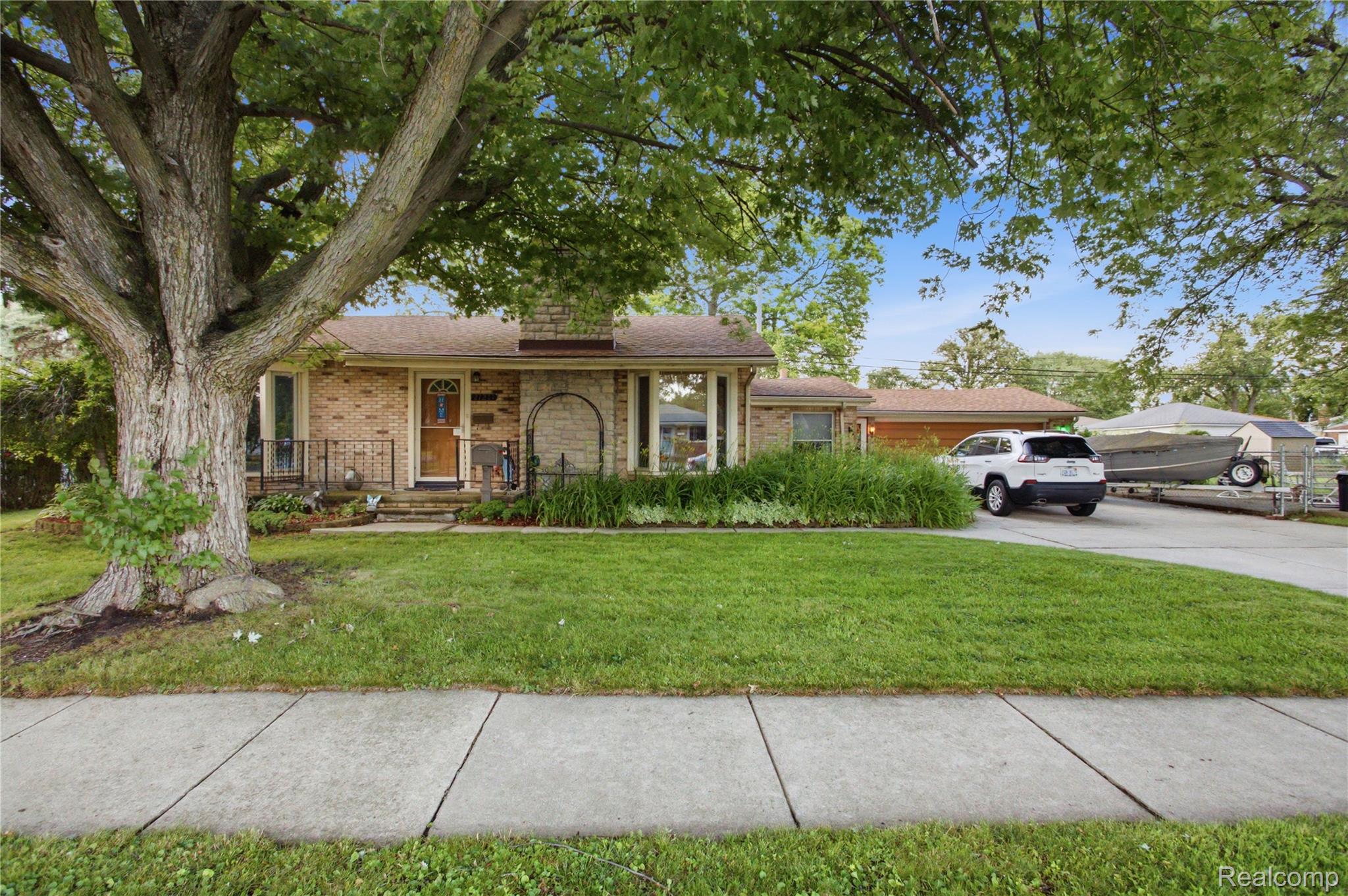 Brick ranch home behind a large mature tree, with a white SUV and boat in the driveway.