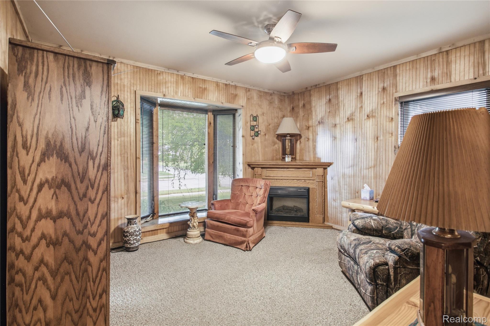 Living room with wood-paneled walls, a fireplace, and a pink armchair beside a camouflage-patterned sofa.