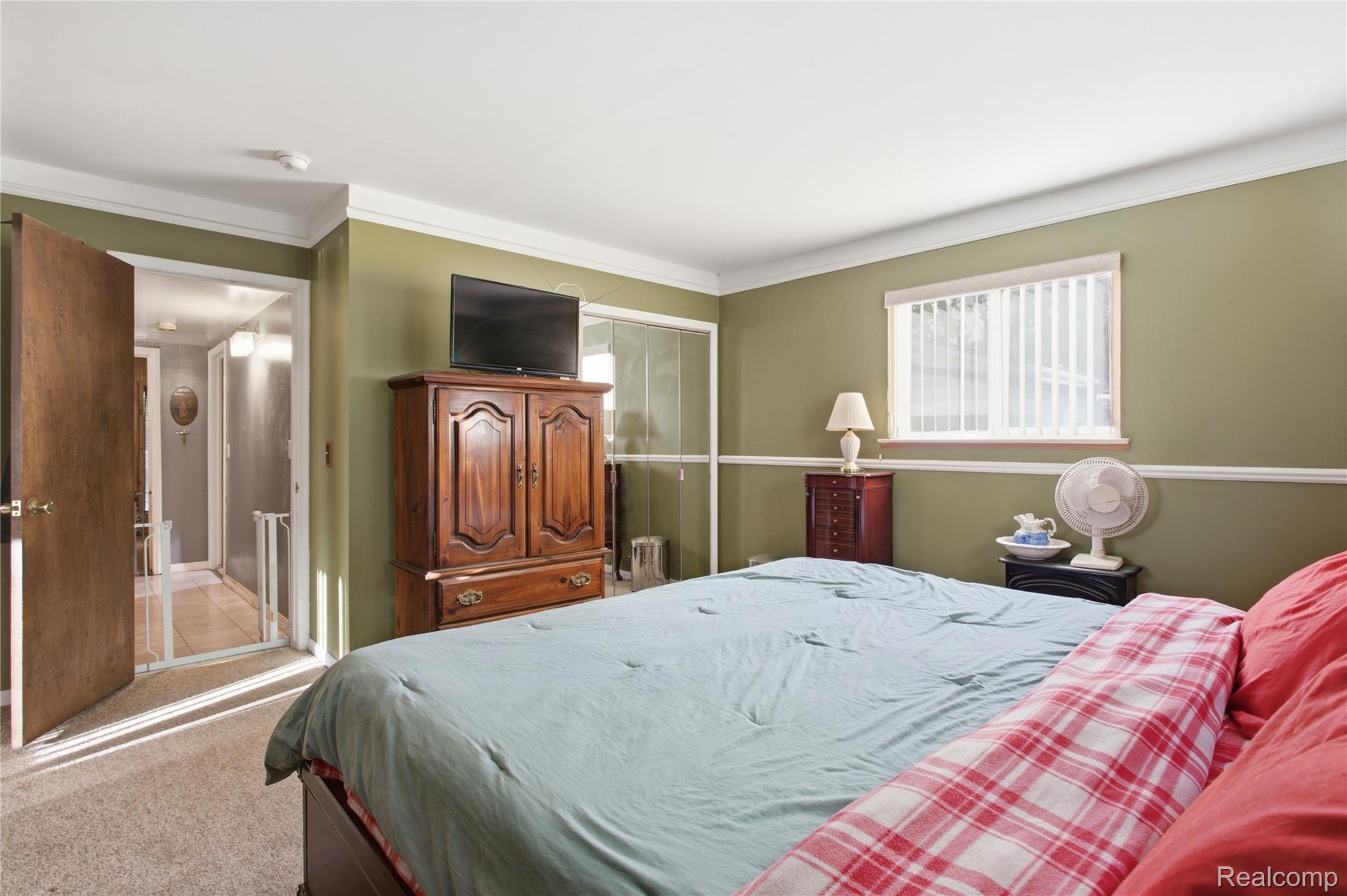 Bedroom with olive-green walls, a large bed, and a wooden armoire topped by a television.