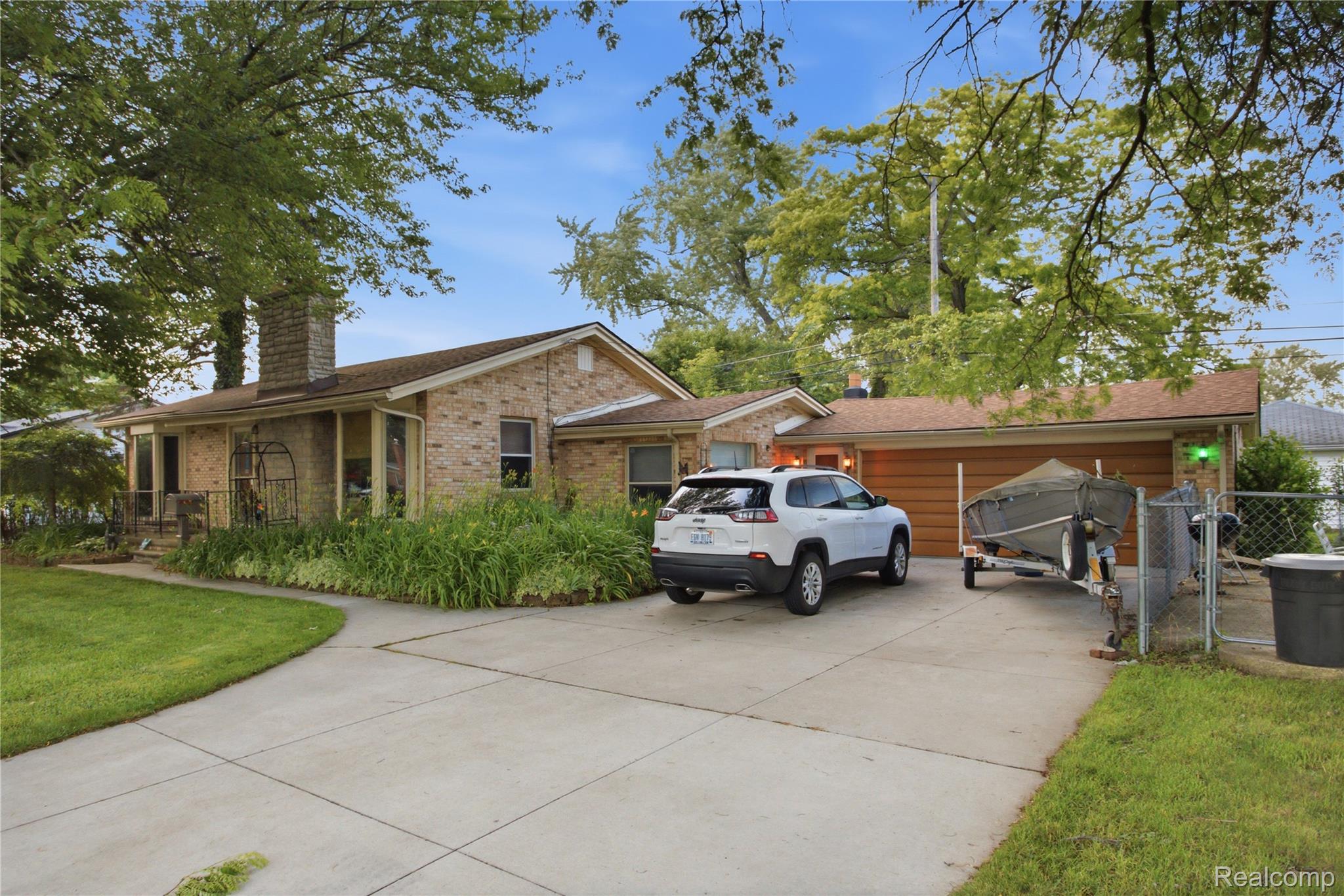 Brick ranch house with a long garage, mature trees, and a boat trailer in the driveway.