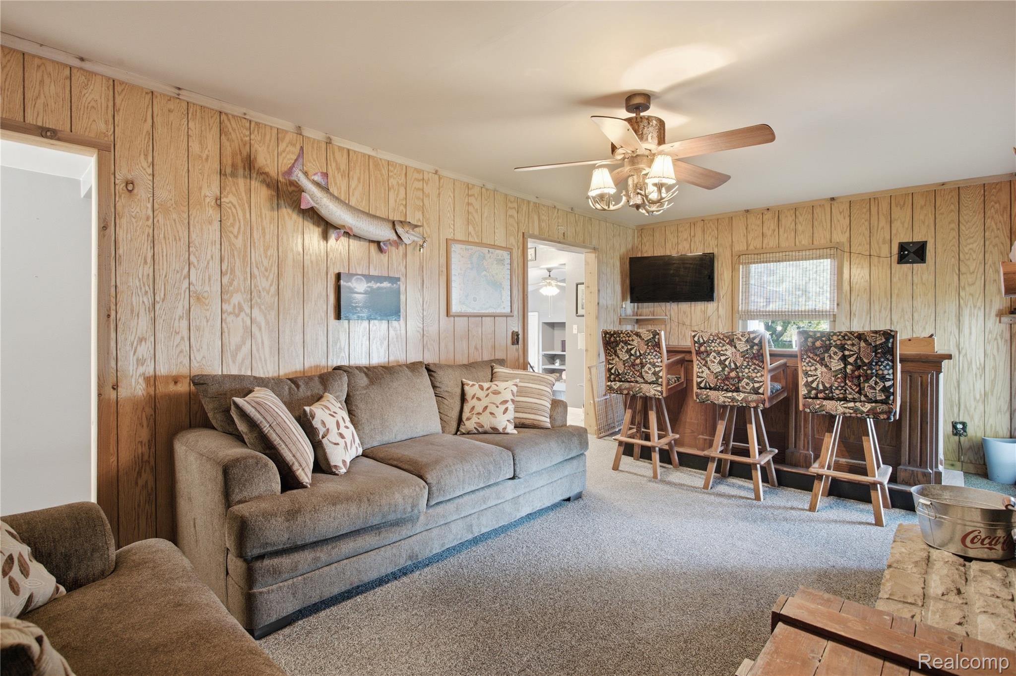 Living room with wood-paneled walls, a gray sectional, and a bar counter with three stools.