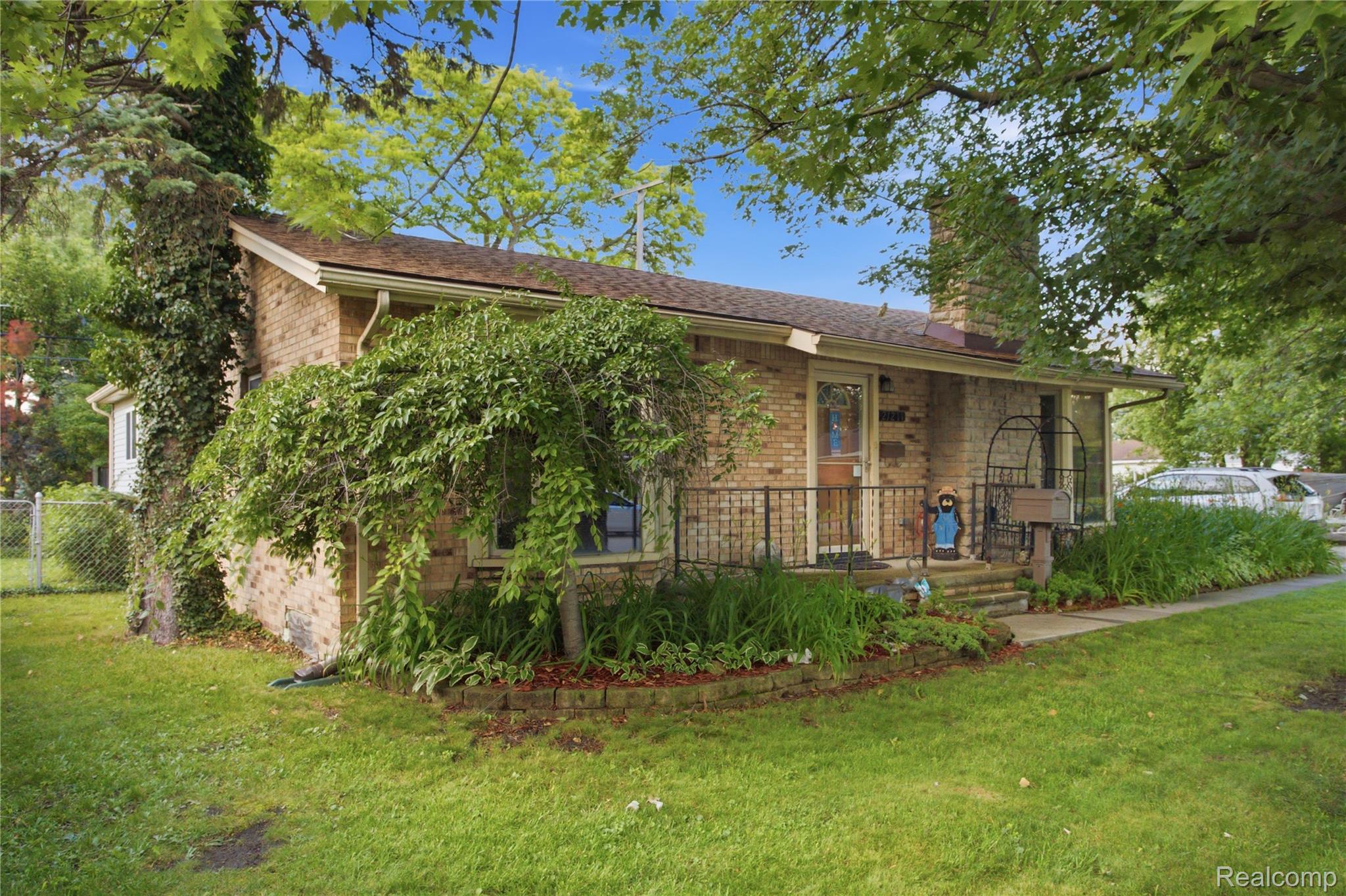 Brick ranch home with a covered entry, mature trees, and a landscaped front yard.